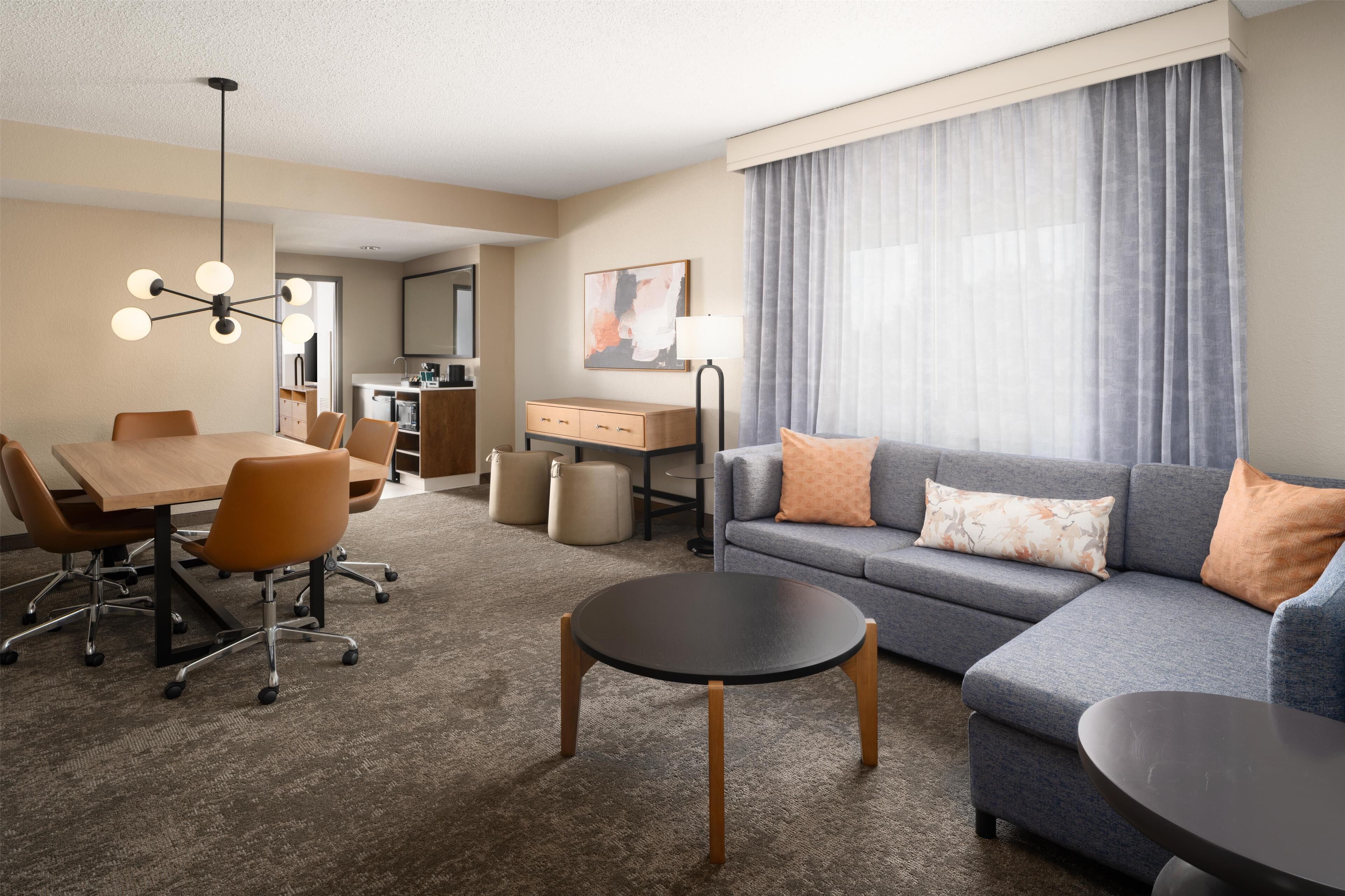 A hotel room with a dining area, a sofa, a round table, and a lamp.