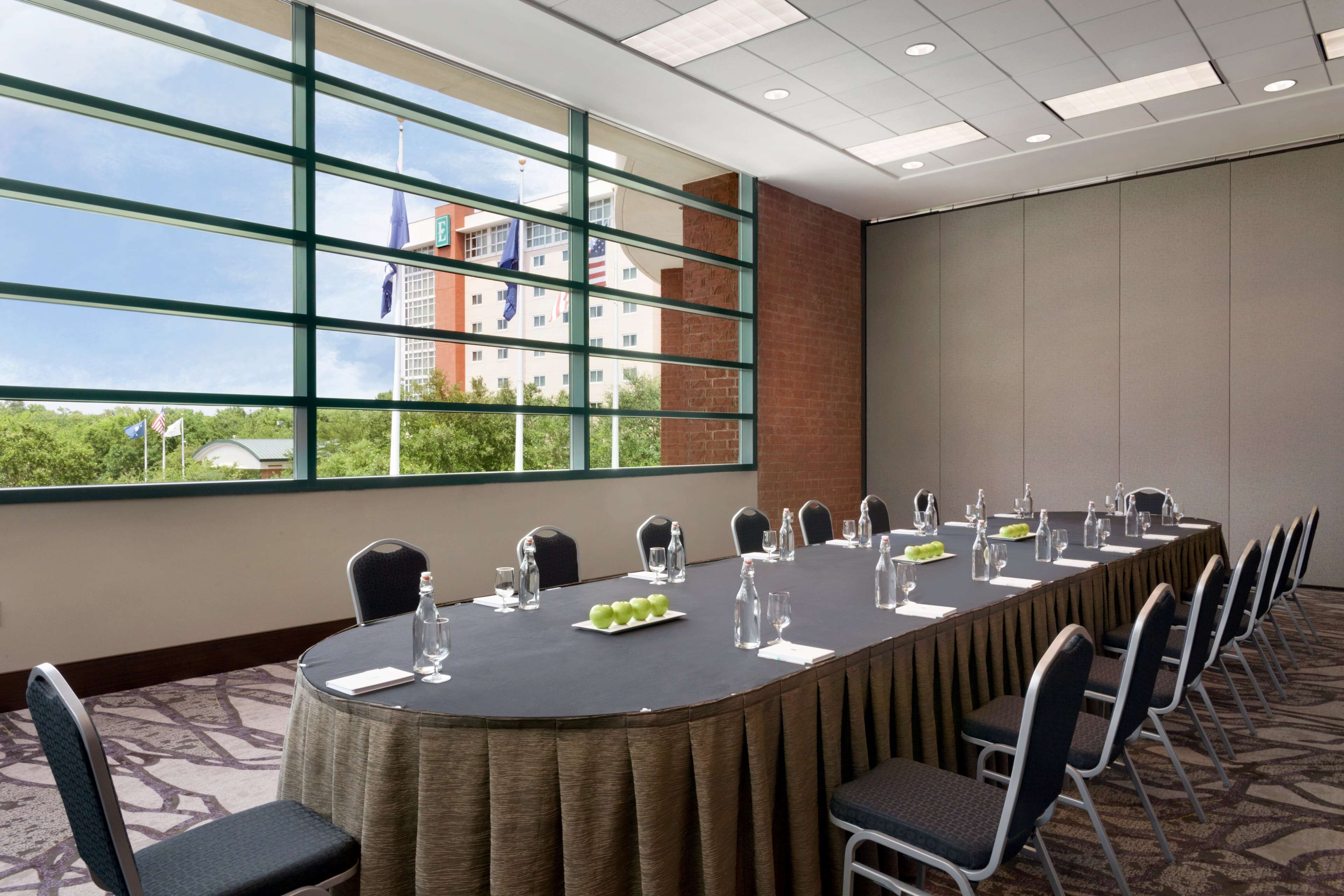 A conference room with a long table, chairs, and a view of a building through large windows.