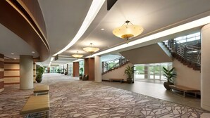 Eine geräumige Lobby mit einem gemusterten Teppich, mehreren Sitzbereichen und einer Treppe zu den oberen Stockwerken.