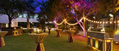 Un espacio para eventos al aire libre con mesas redondas, luces colgantes y faroles.