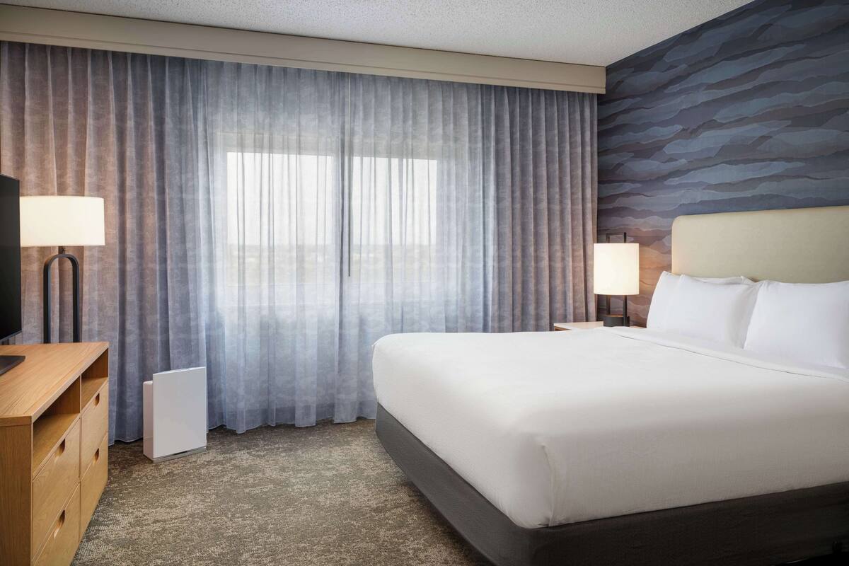 A hotel room with a large bed, two bedside lamps, a flat-screen TV, a wooden dresser, and a radiator.