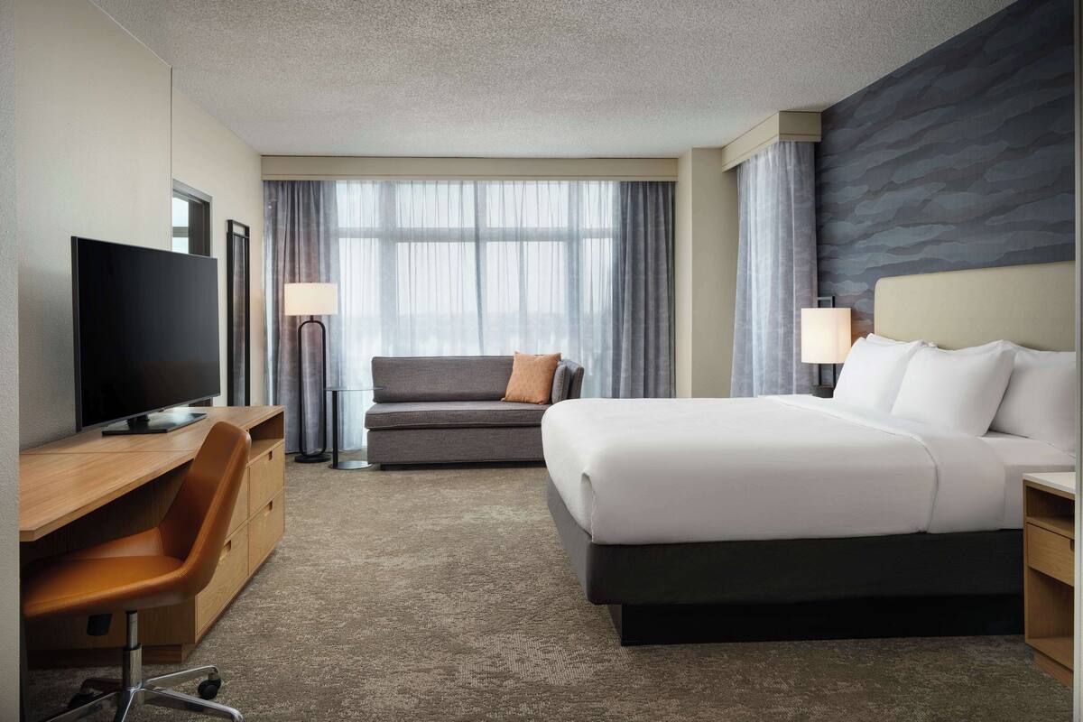 Una habitación de hotel con una cama, un sofá, un escritorio con televisor y una lámpara.
