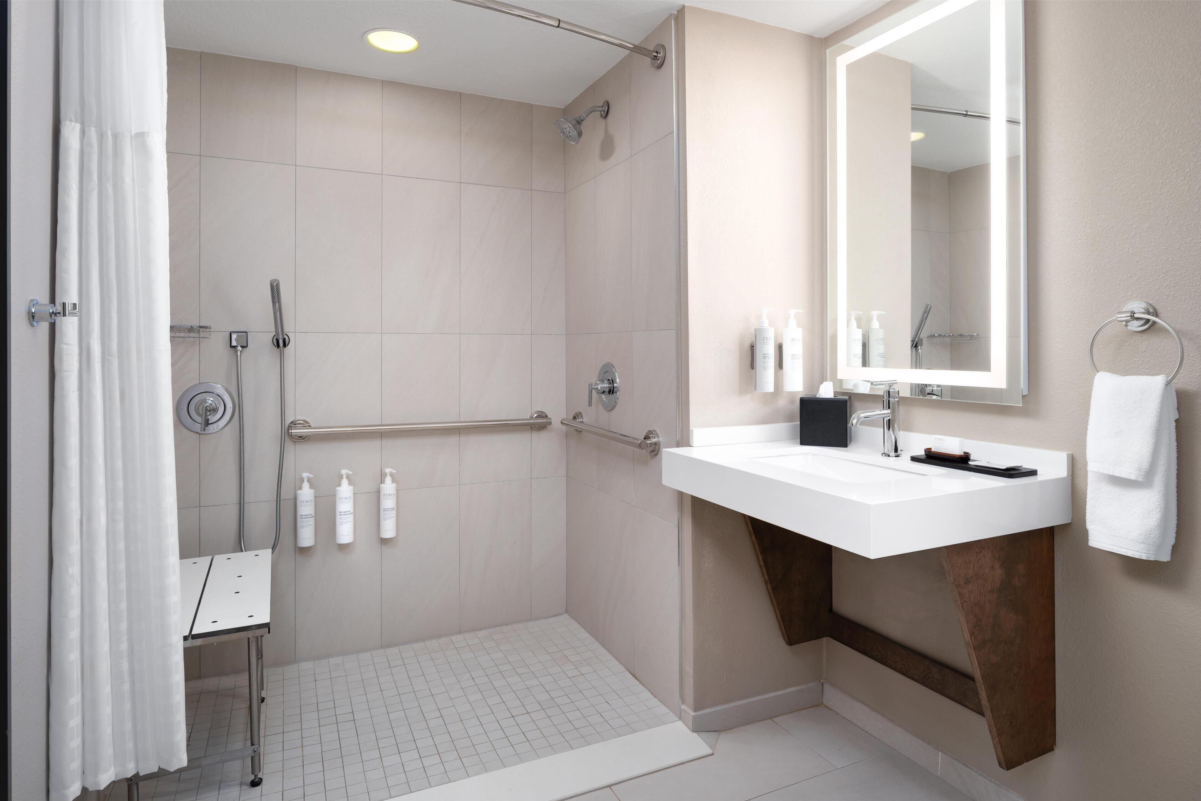 Een moderne badkamer met een douche, handgrepen, een wastafel en een grote spiegel.