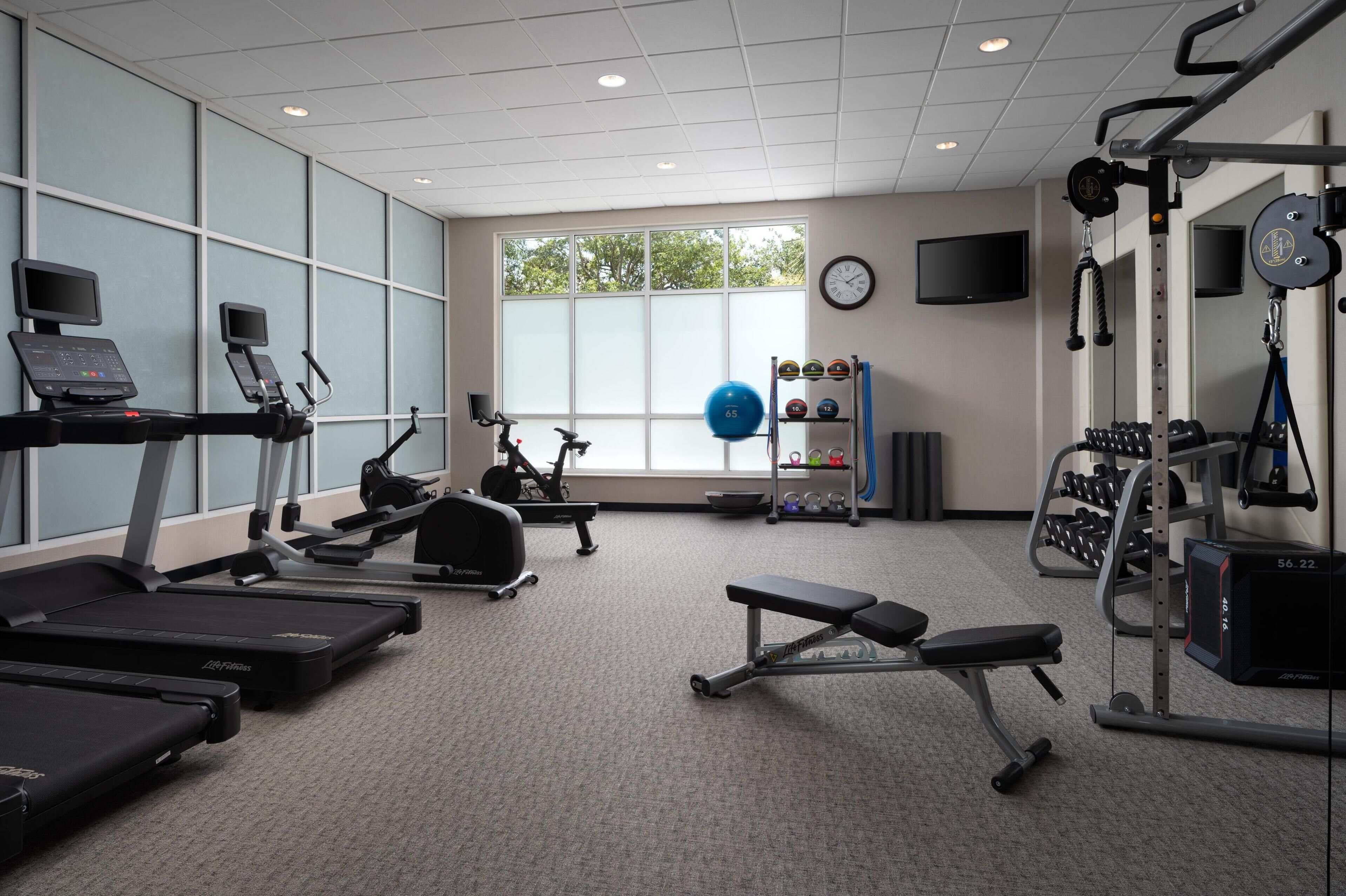 A gym with treadmills, a bench, weight machines, and a window with a view of trees.