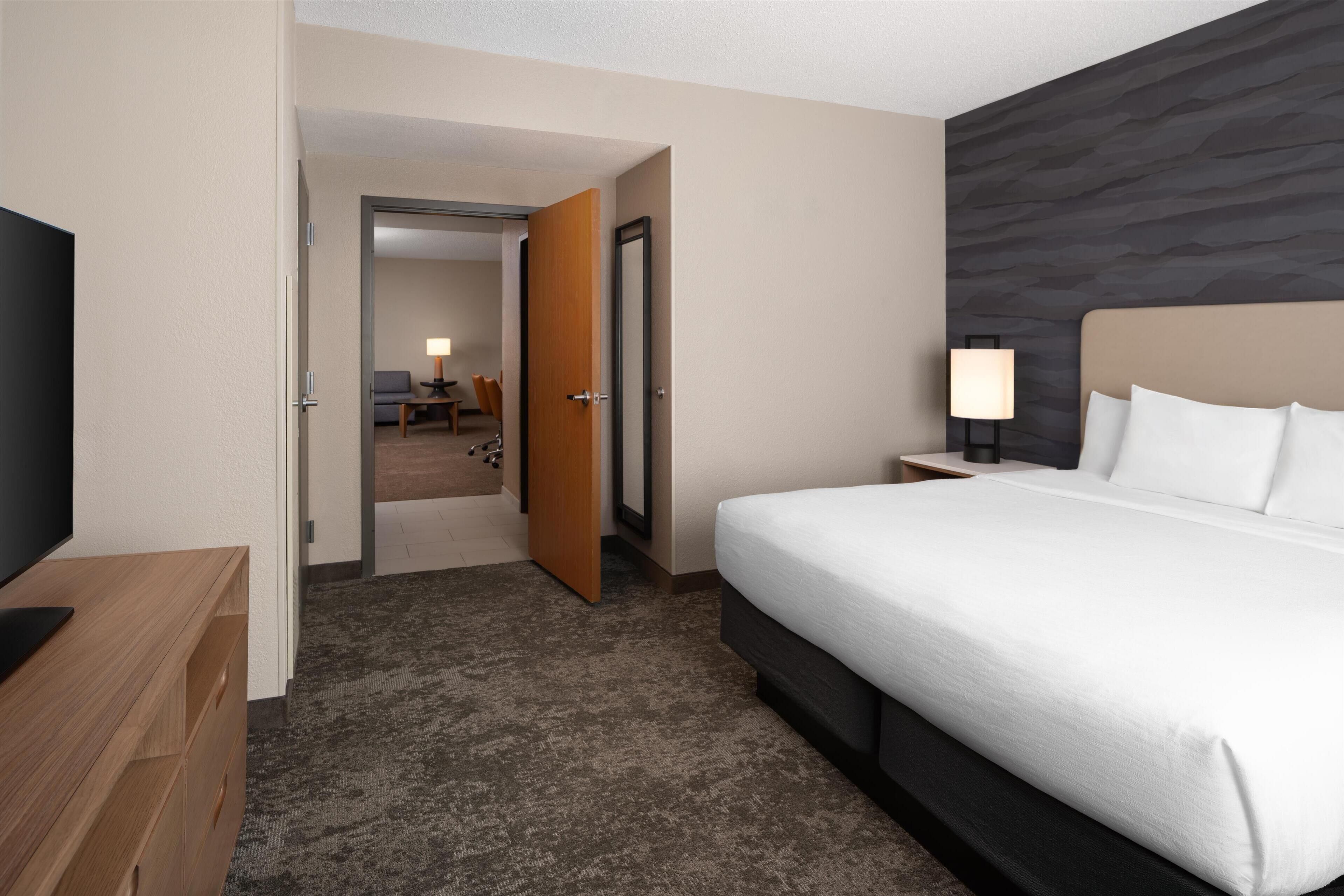 Hotelkamer met een groot bed, een televisie, een houten dressoir en een zichtbare badkamer door een open deur.
