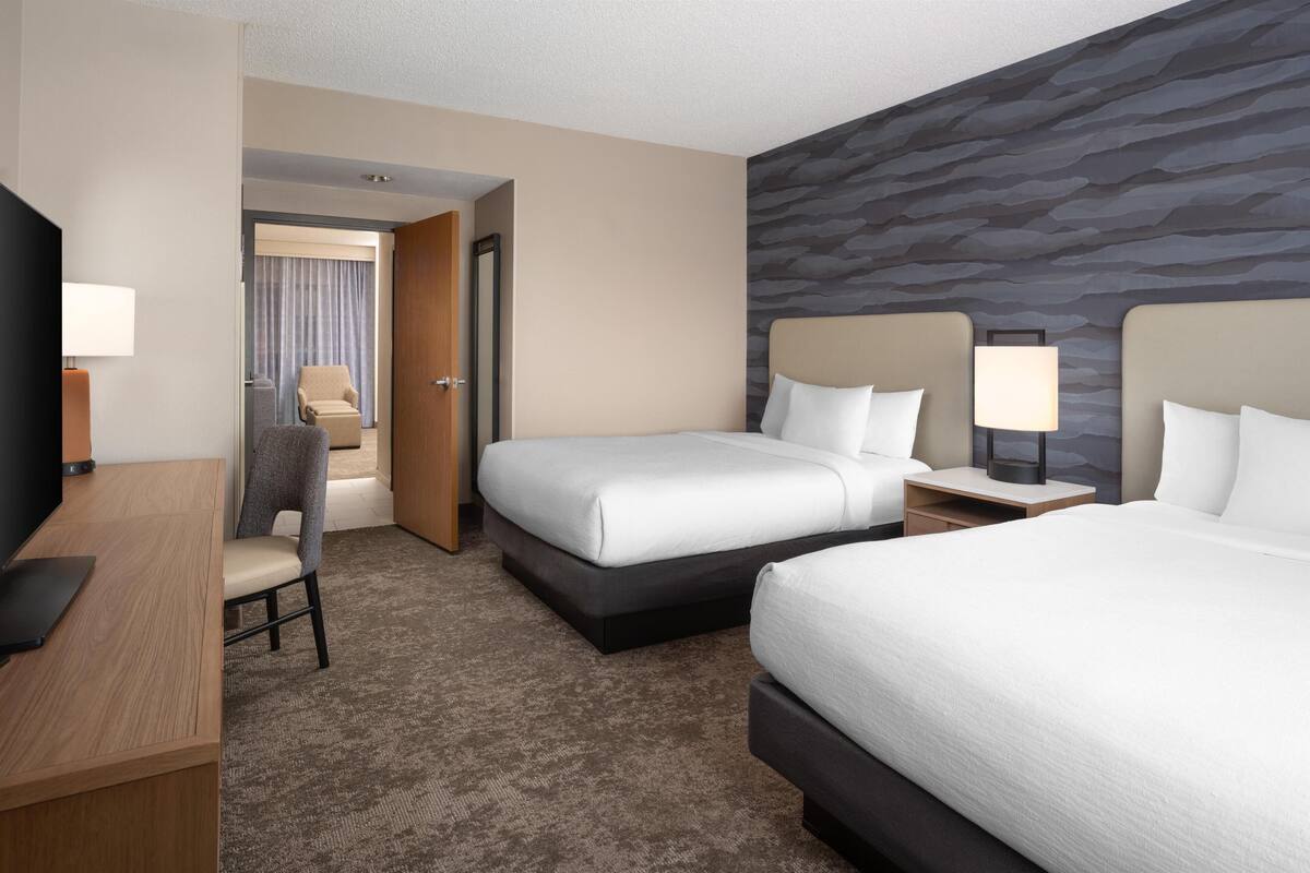 A hotel room with two beds, a desk, a chair, and a TV.