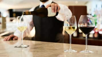 A bar setting with a person pouring wine into glasses, three glasses on the counter, and a blurred background.