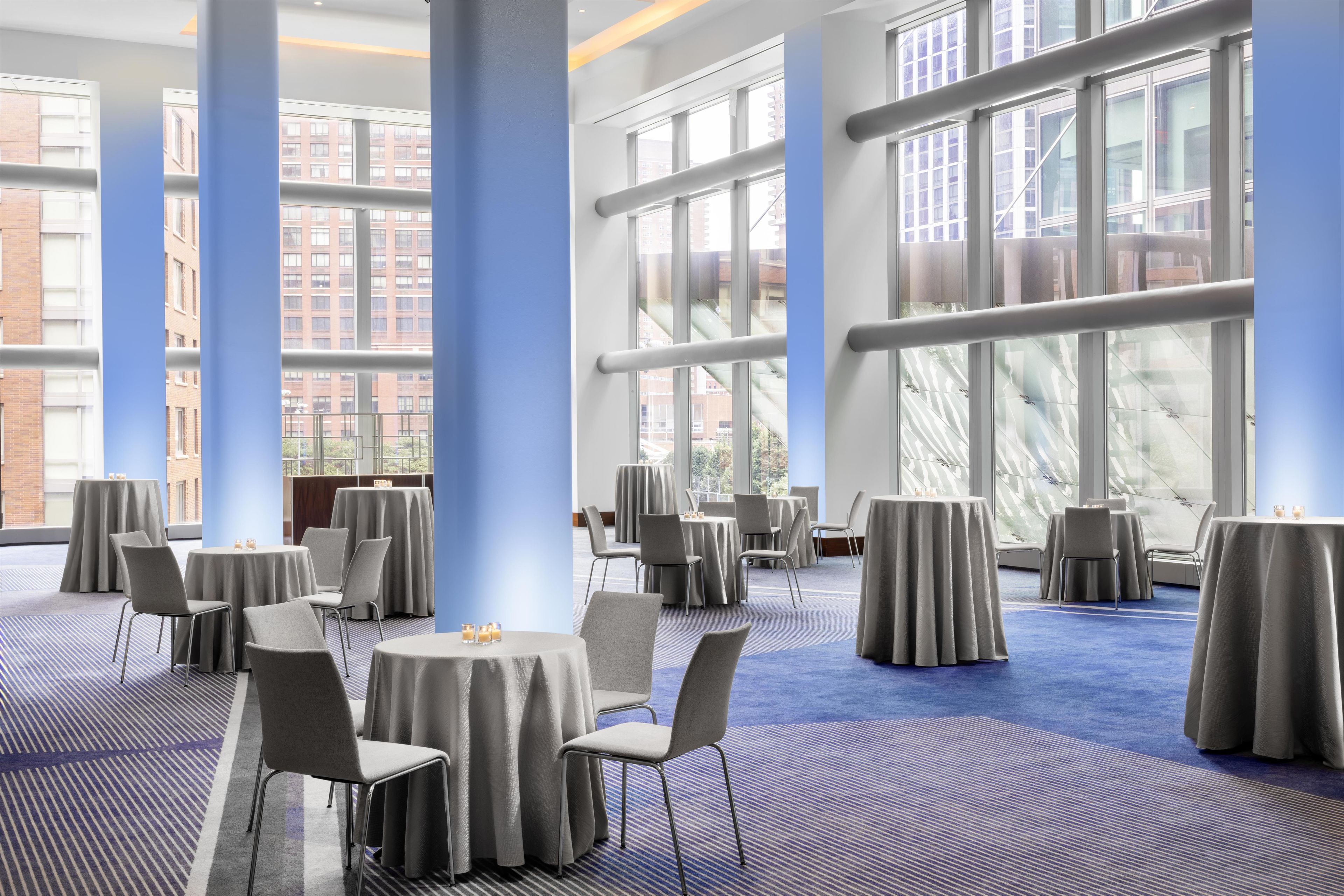 A spacious conference room with round tables, chairs, and large windows offering views of the cityscape.