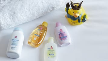 Four baby care products on a white surface with a plush white towel and a yellow duck figurine.