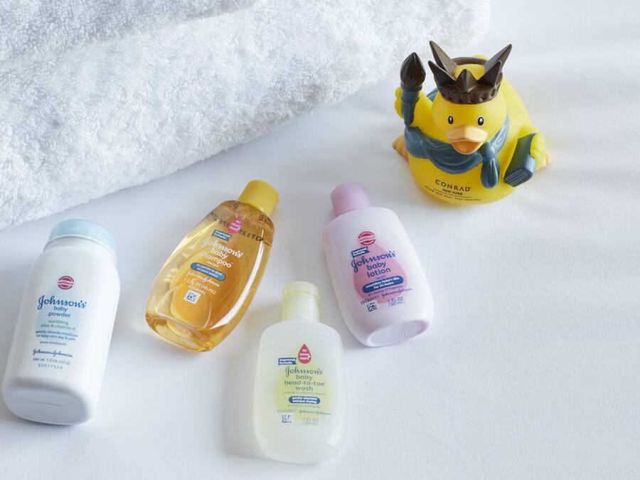 Quatre productes per a nadons sobre una superfície blanca, amb una tovallola blanca mullada i una figura de pato groc.