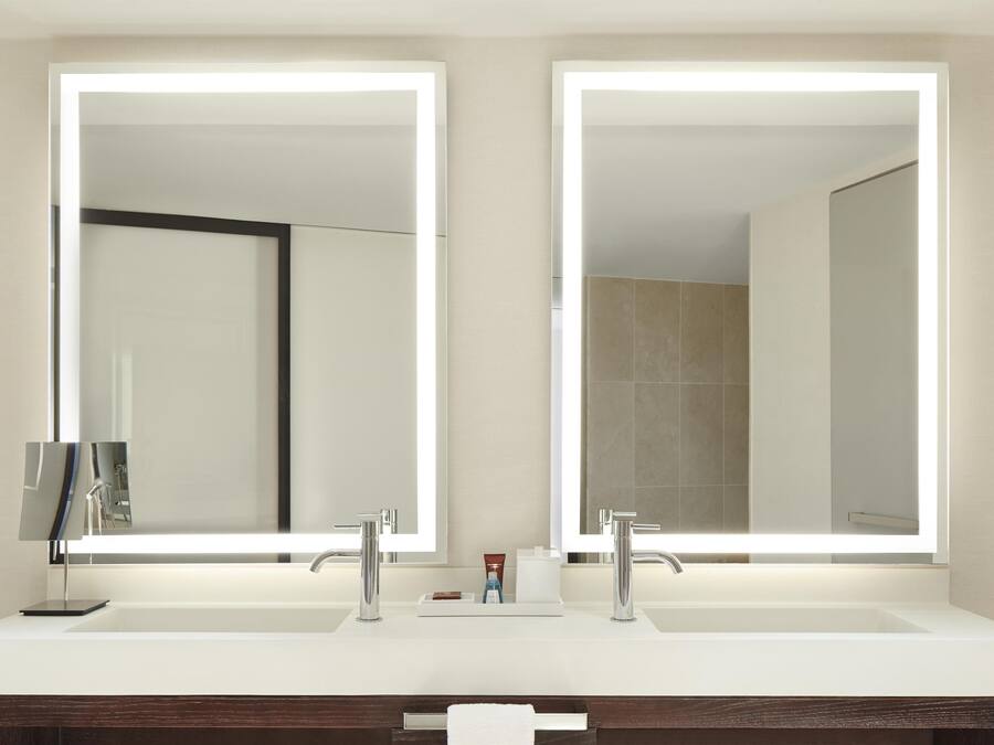 Un baño con lavamanos doble, dos espejos grandes y un mueble de tocador de madera oscura.