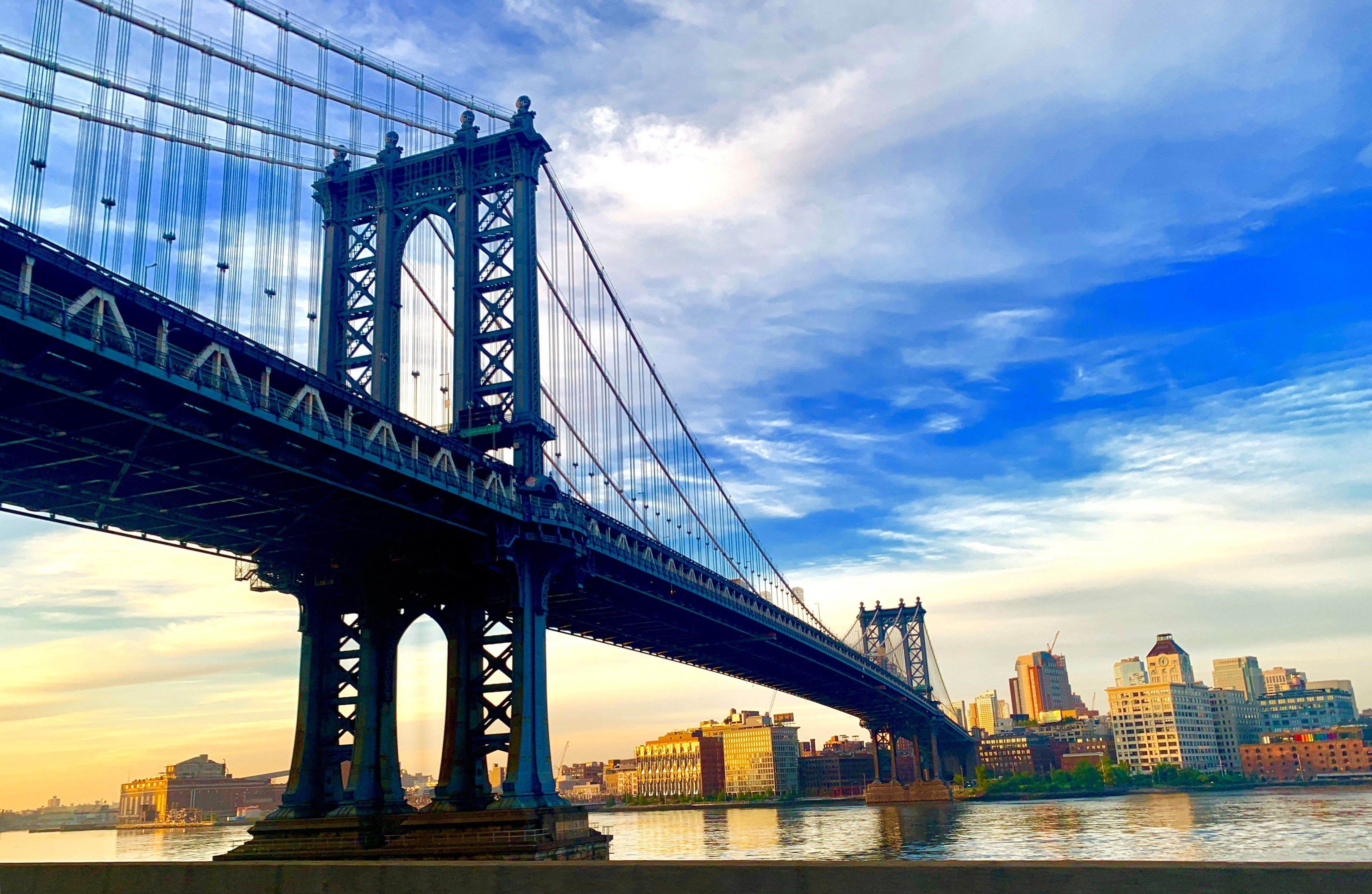 A large suspension bridge with multiple towers and cables, spanning over a body of water with a city skyline in the background.