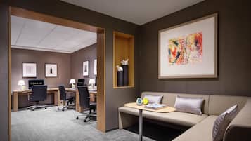 Habitación de hotel con sofá, una mesita, escritorio con dos sillas, computadora y cuadros en la pared.