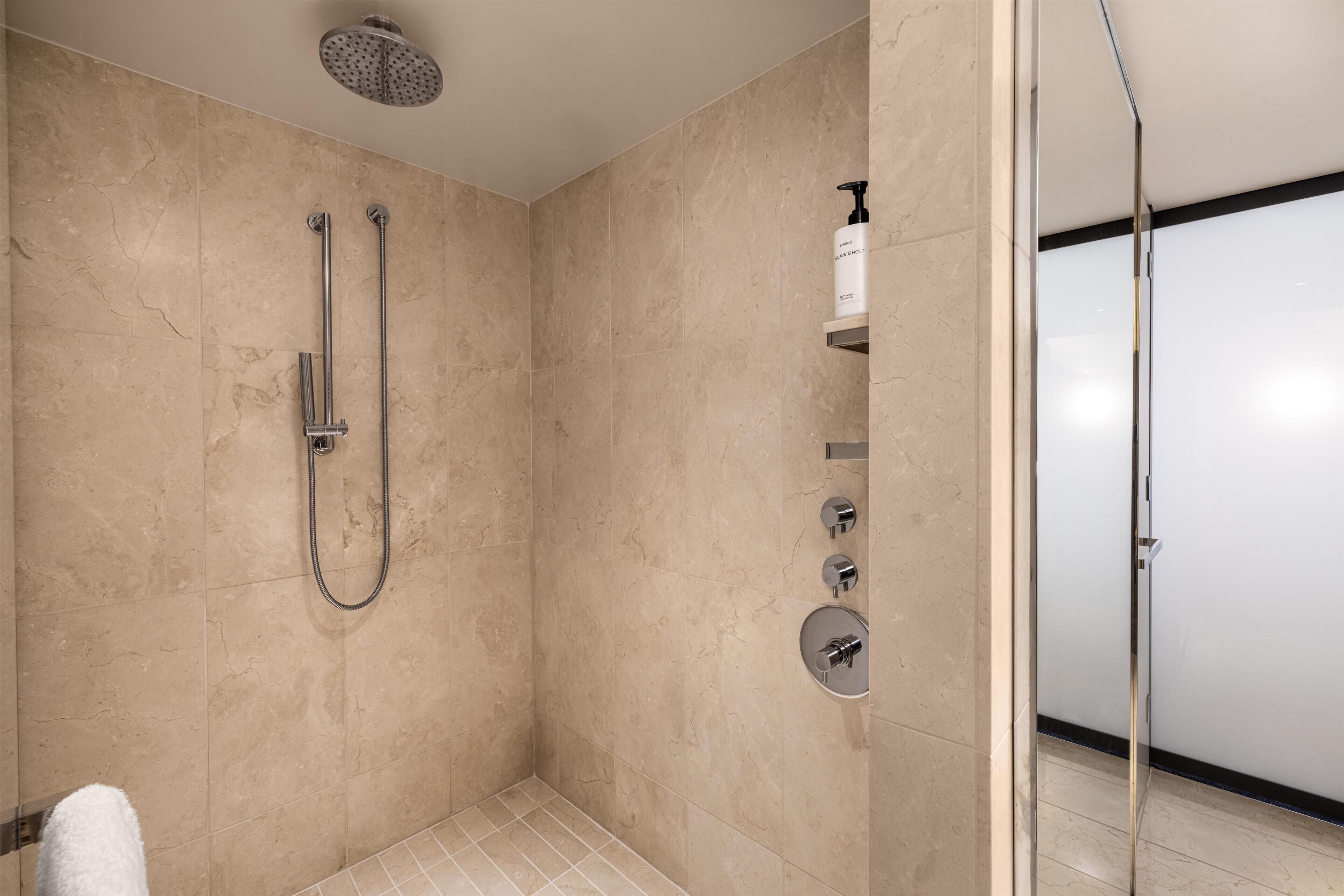 A modern bathroom with a glass shower enclosure, a handheld showerhead, a wall-mounted faucet, and a soap dispenser.