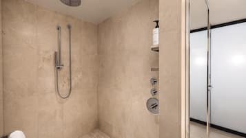 A modern bathroom with a glass shower enclosure, a handheld showerhead, a wall-mounted faucet, and a soap dispenser.