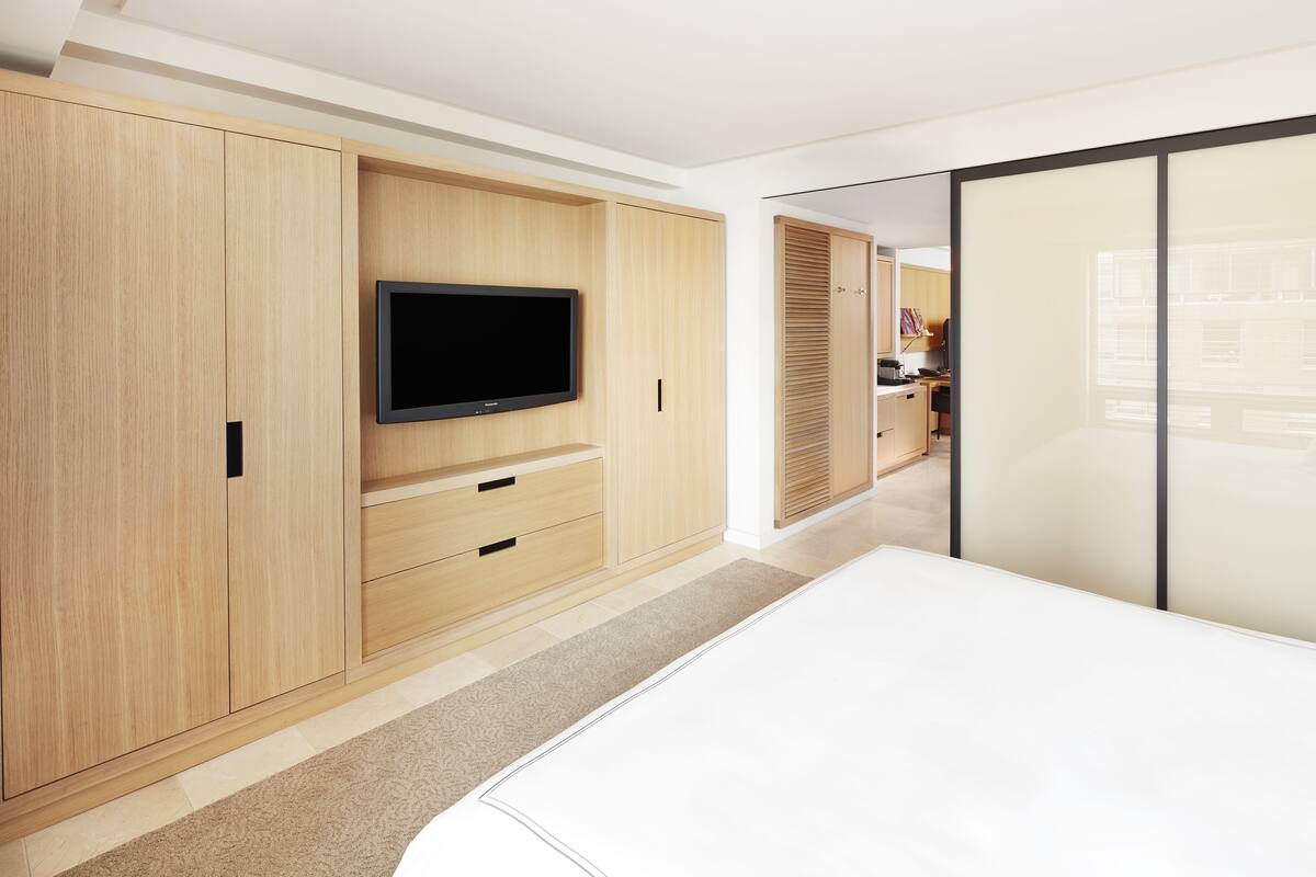 A modern bedroom with a large bed, wooden wardrobe, and a flat-screen TV.