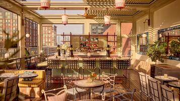A rooftop bar with multiple seating areas, a bar counter with bottles, and a view of the cityscape.