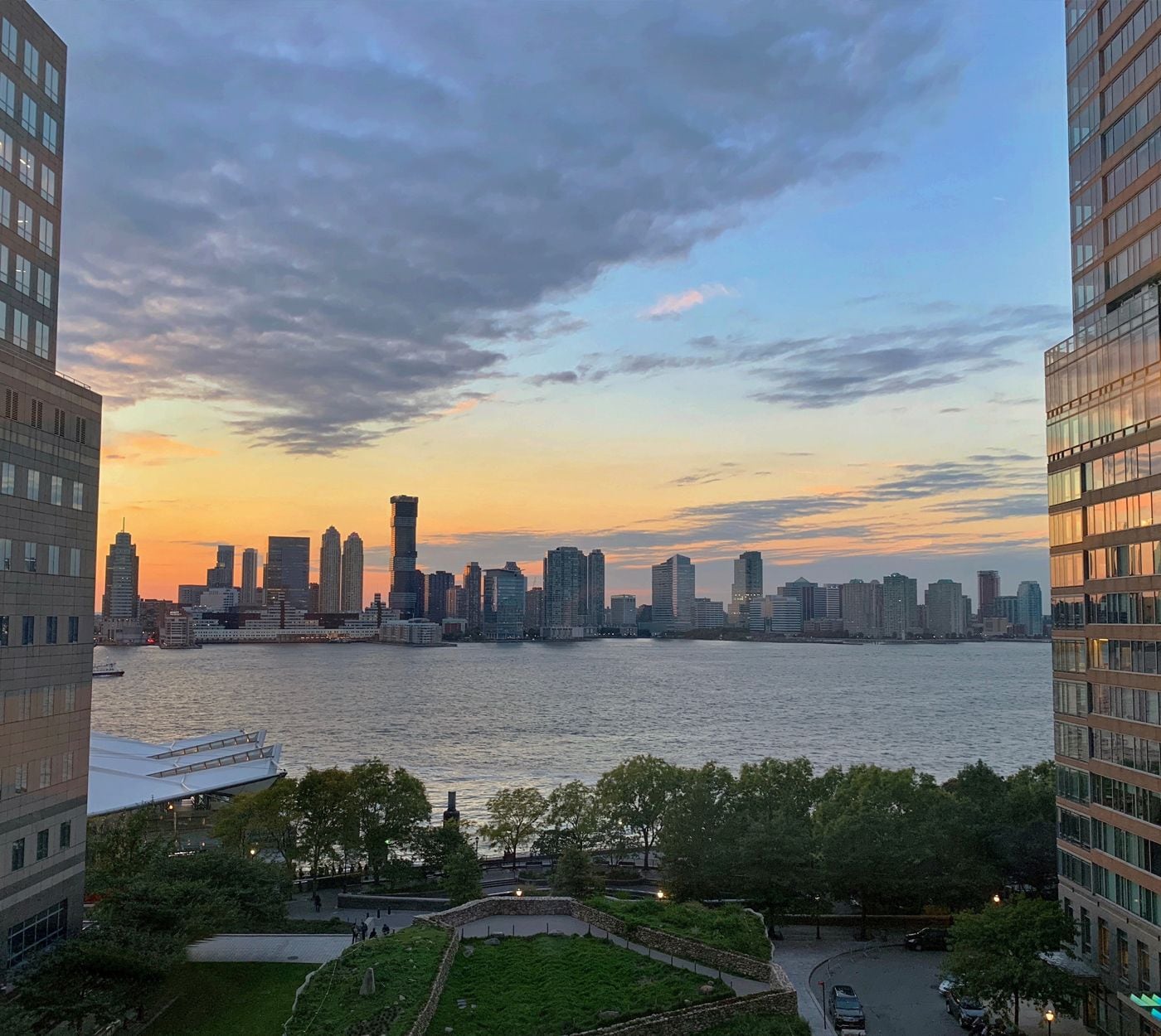 Une vue sur les gratte-ciel d’une ville au coucher du soleil, avec une rivière au premier plan et des immeubles de grande hauteur de chaque côté.