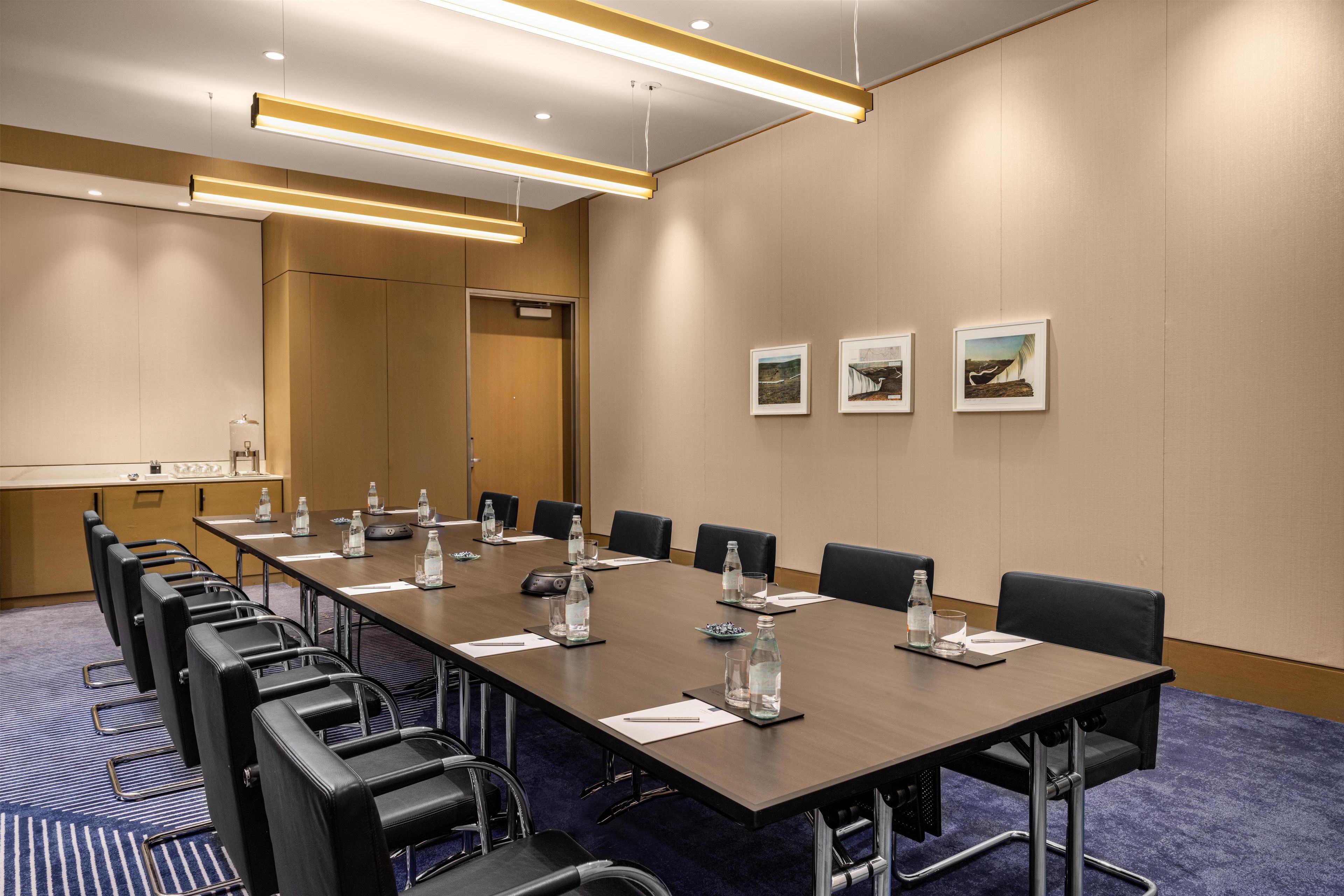 A conference room with a long table, chairs, water bottles, and framed pictures on the wall.