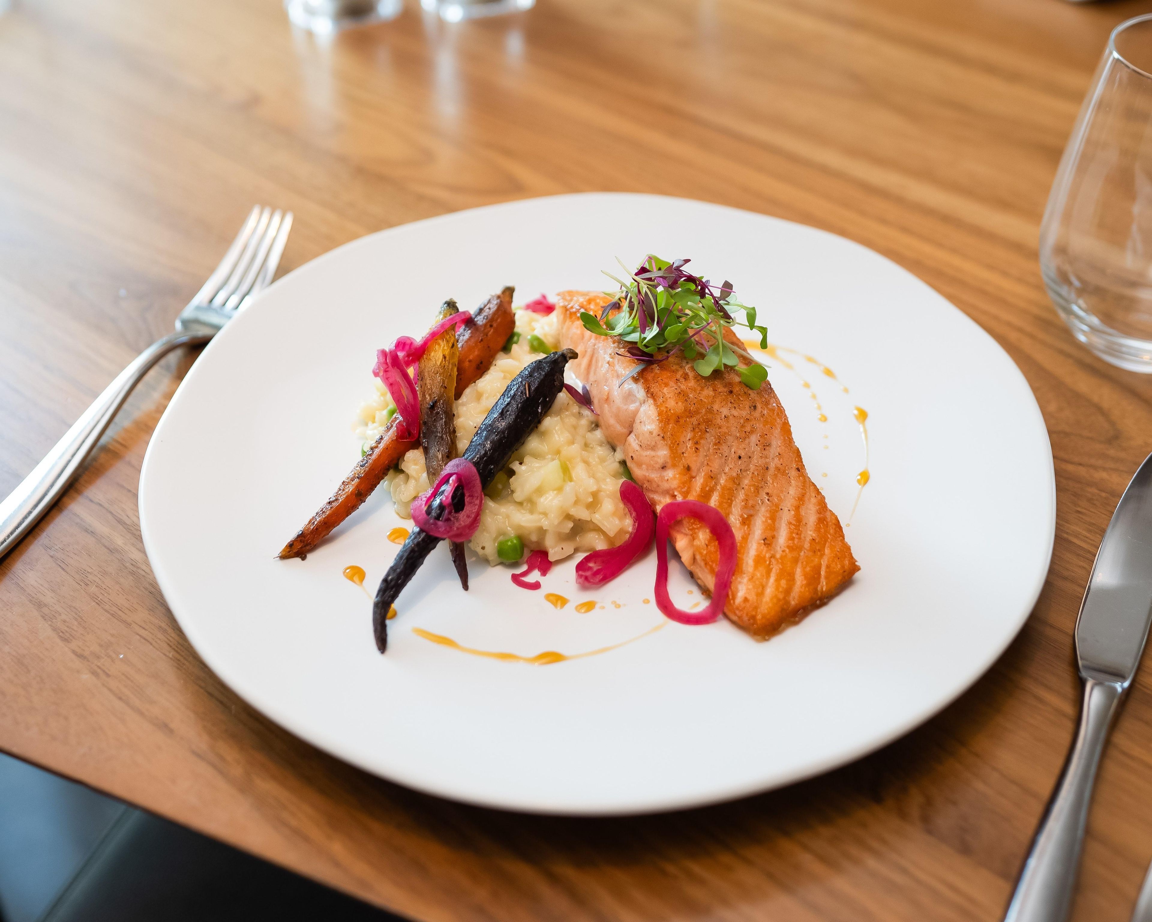A plate of food with salmon, vegetables, and a sauce on a white plate.