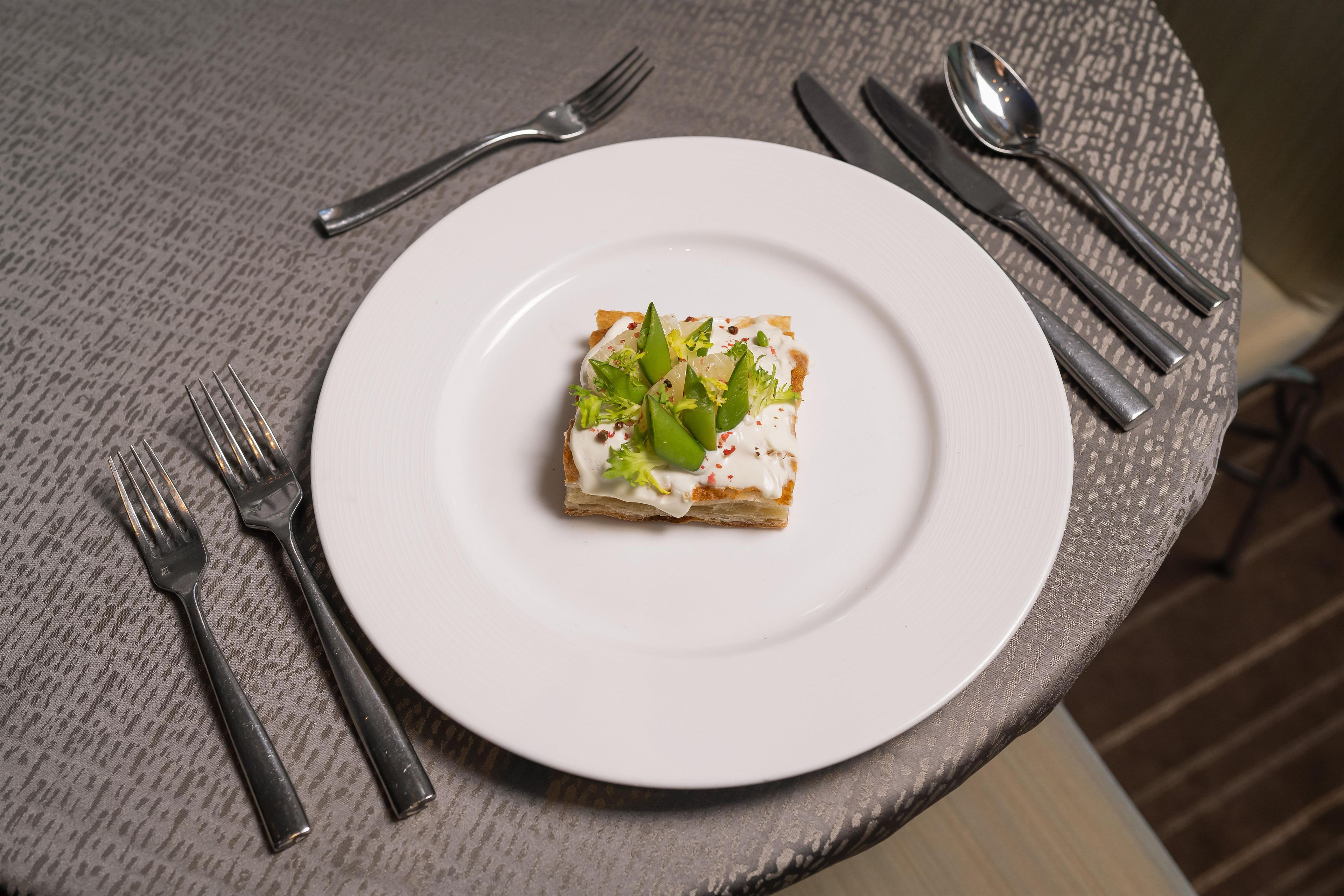 A plate with a piece of food on a table with cutlery.