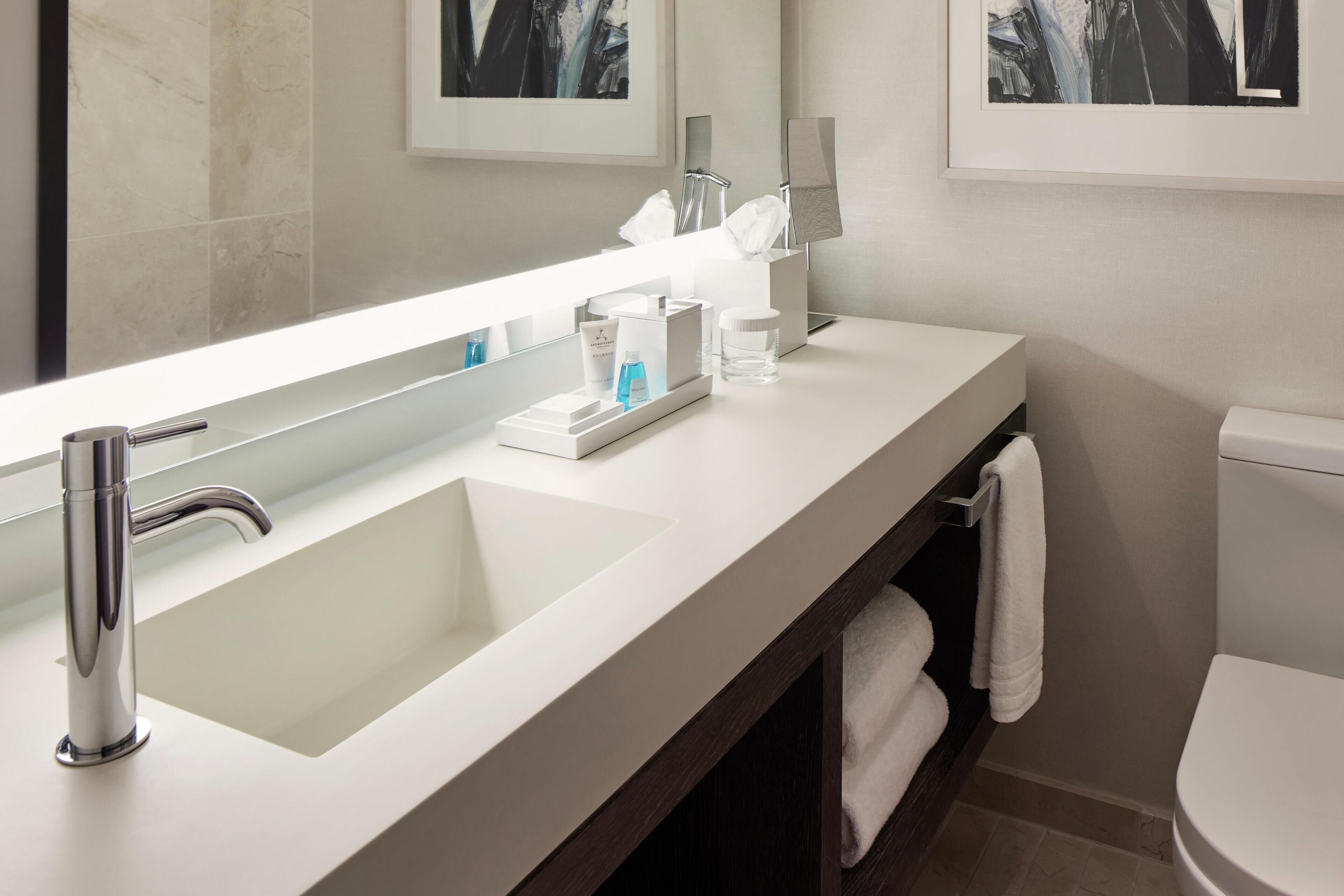 A modern bathroom with a large mirror, a white sink, a toilet, and a towel rack.