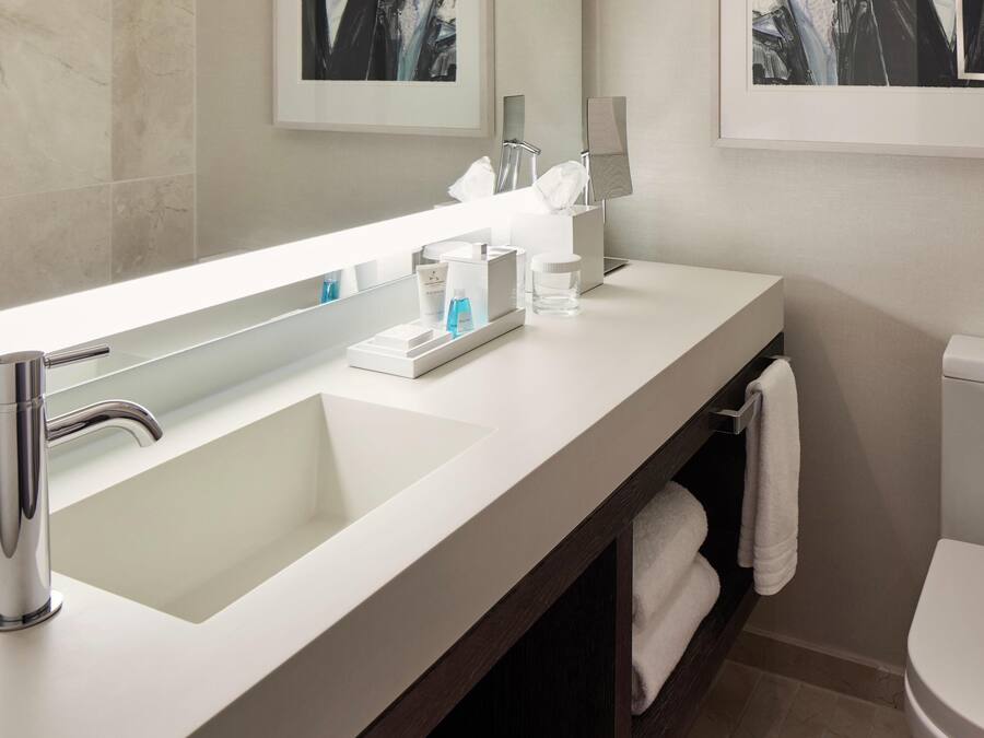 A modern bathroom with a large mirror, a white sink, a toilet, and a towel rack.