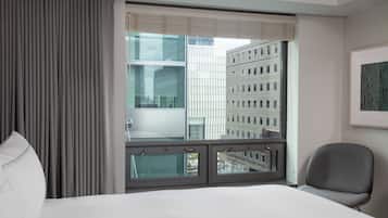 A hotel room with a large window, a bed, a chair, and a framed picture on the wall.