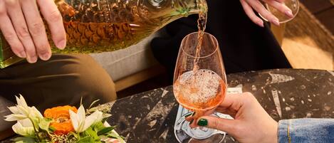 A person pouring a drink into a glass, a table with a green cloth, and a vase with flowers.