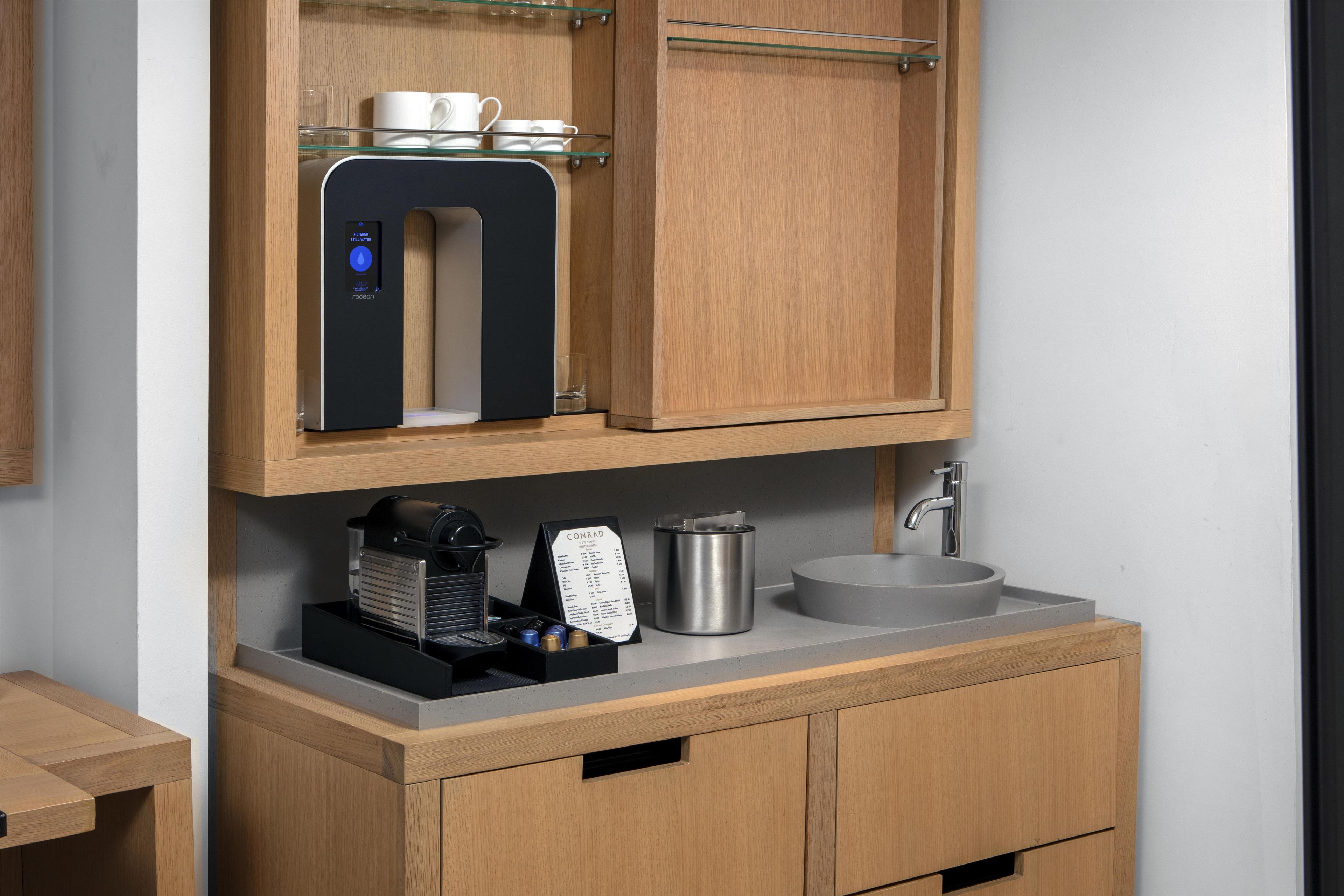 A compact kitchenette with a coffee machine, a water dispenser, and a stainless steel sink.