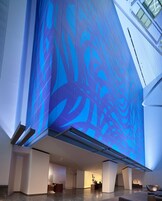 A spacious lobby with a large digital screen displaying abstract patterns, a reception desk, and a high ceiling with skylights.