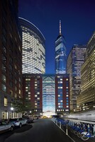 A modern urban street with high-rise buildings, a prominent curved building with a glass facade, and a row of bicycles parked along the sidewalk.