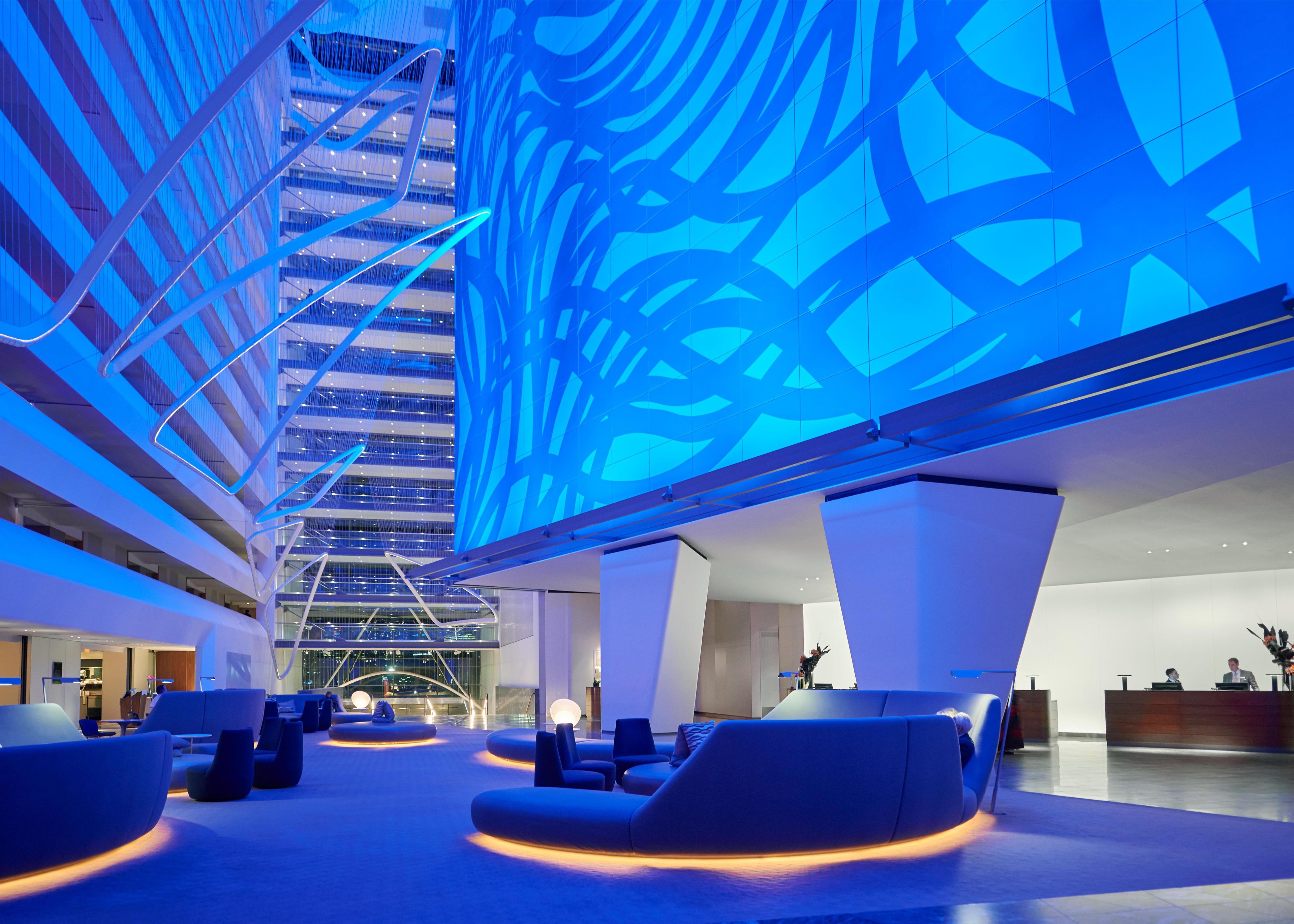 A modern hotel lobby with a high ceiling, a glass atrium, and seating areas.