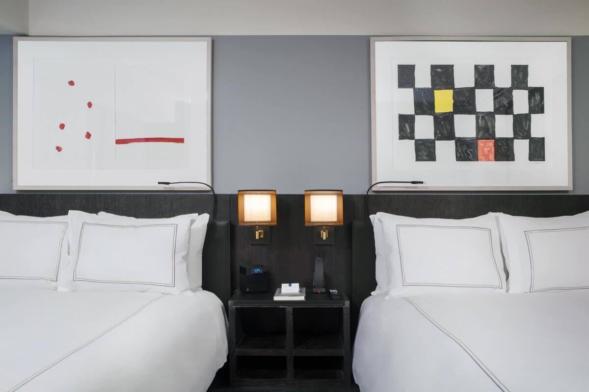 A hotel room with two beds, a nightstand with a clock, and two wall-mounted lamps.