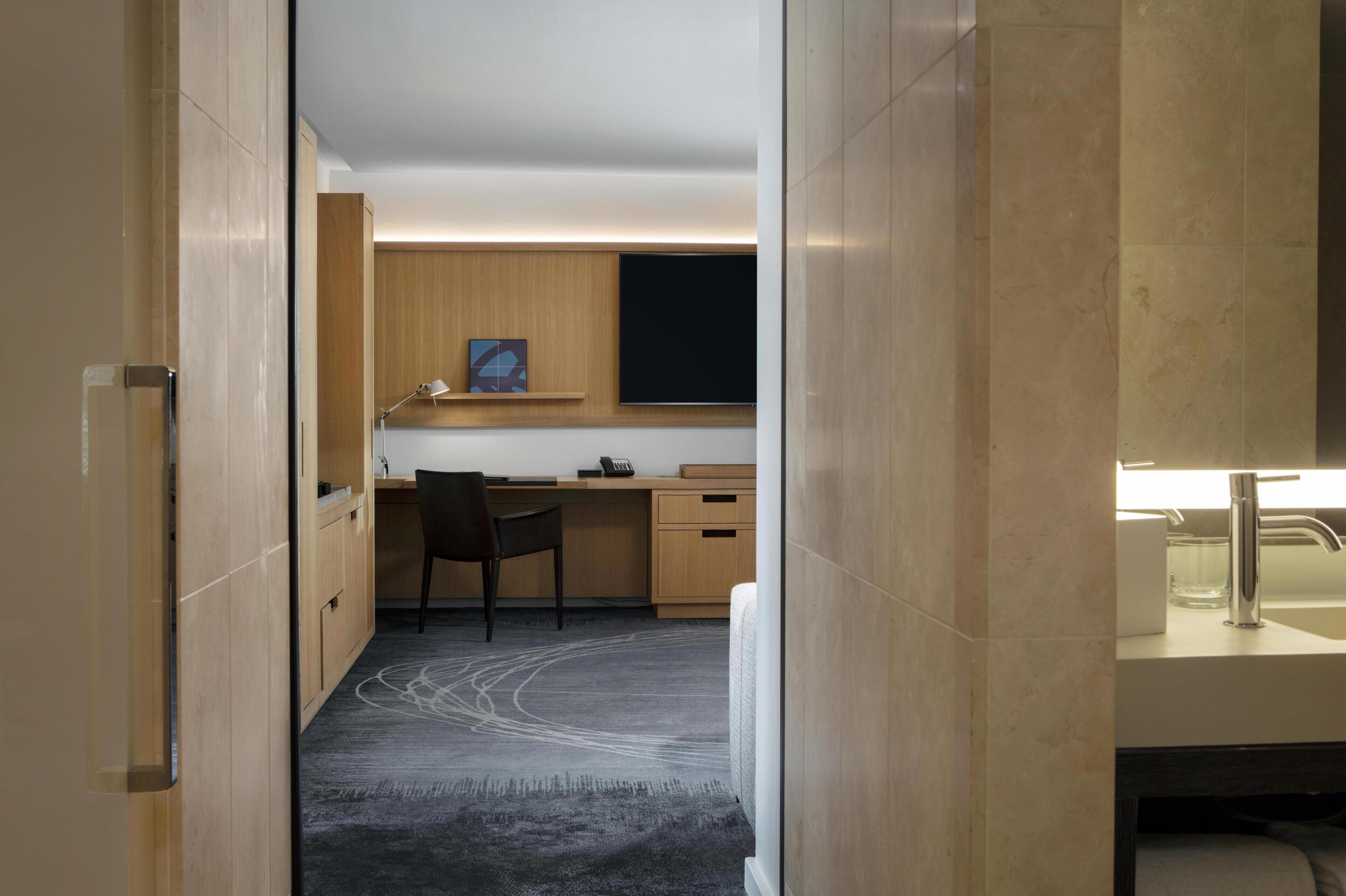 A modern hotel room with a desk, chair, and a large mirror.