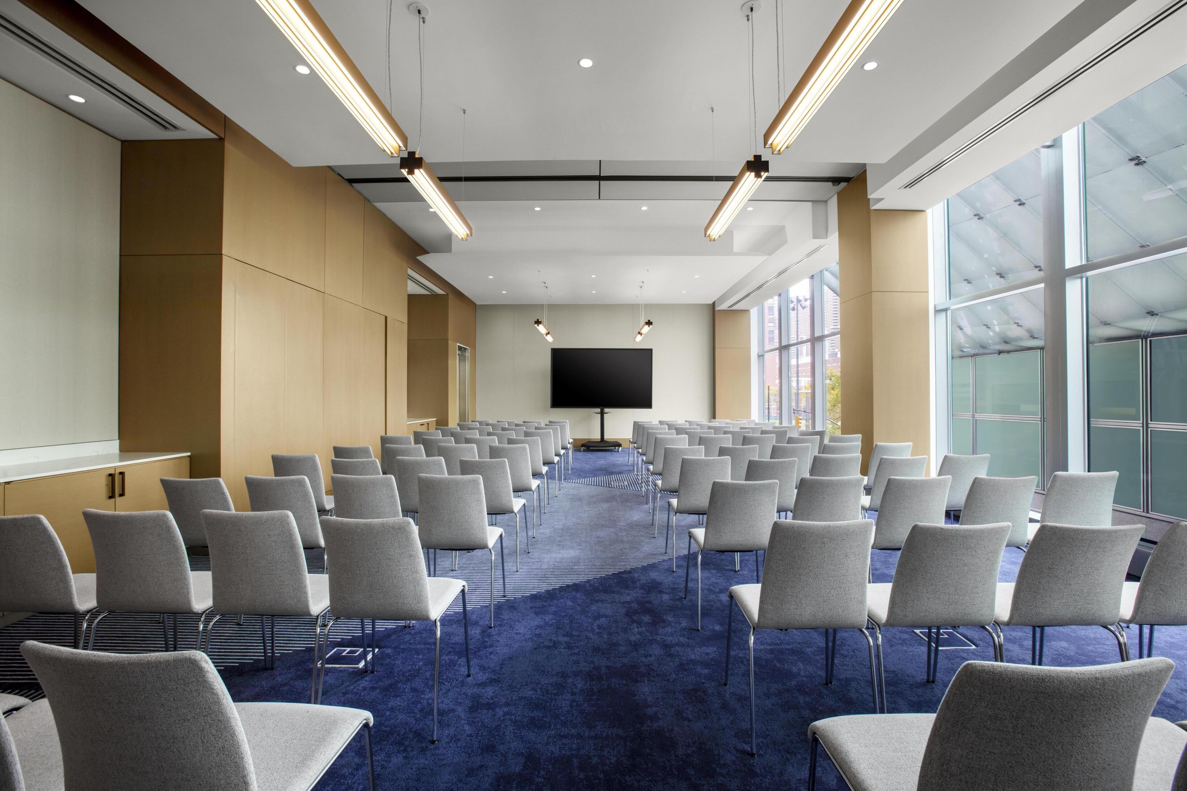 A conference room with rows of chairs, a large screen, and a blue carpet.