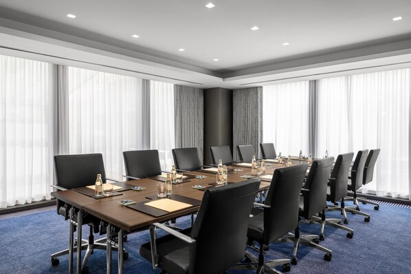 A conference room with a long table, black chairs, and a blue carpet. - Conrad New York Downtown (New York)
