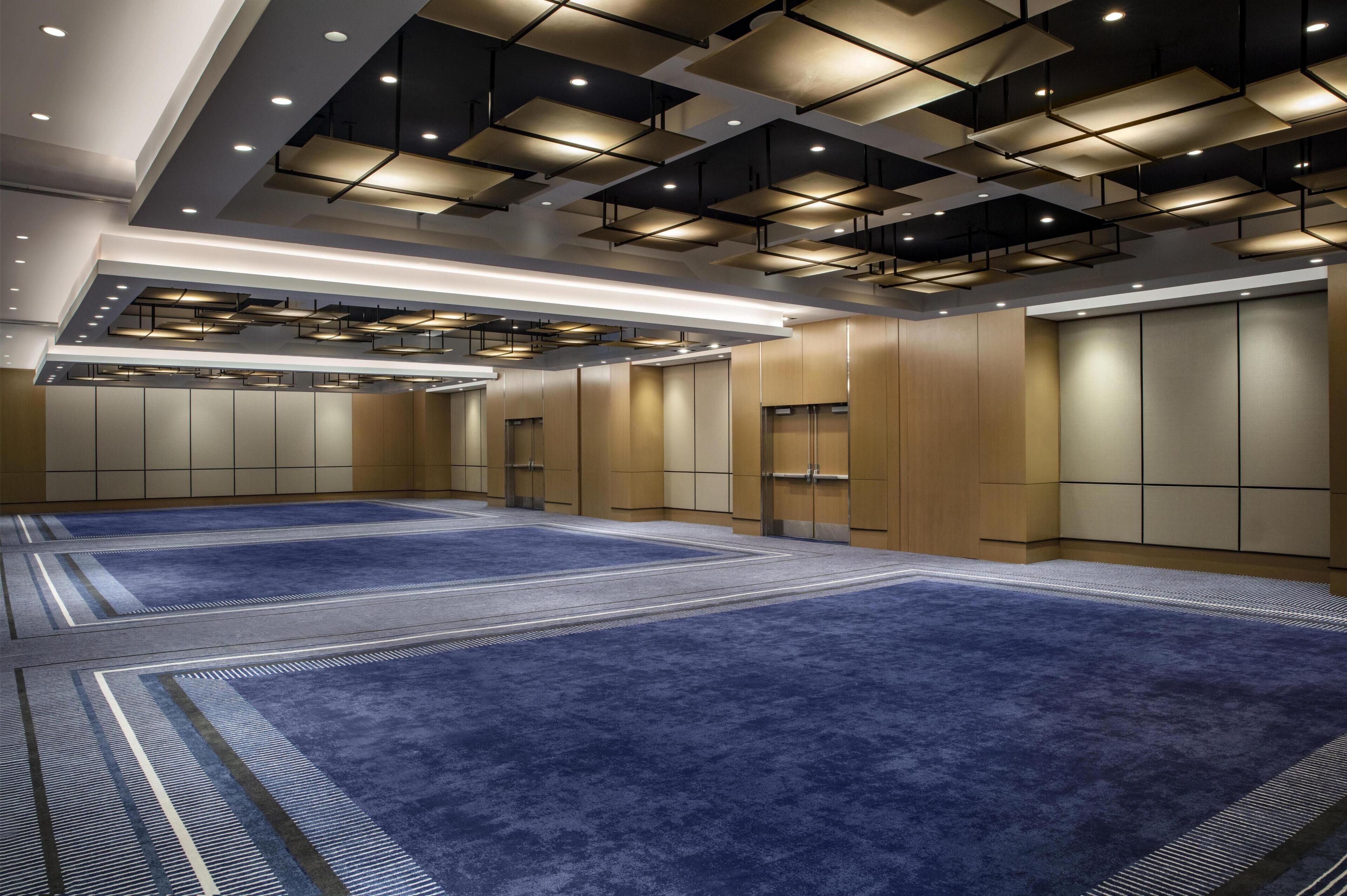 A spacious room with a blue carpet, recessed lighting, and a modern ceiling design.