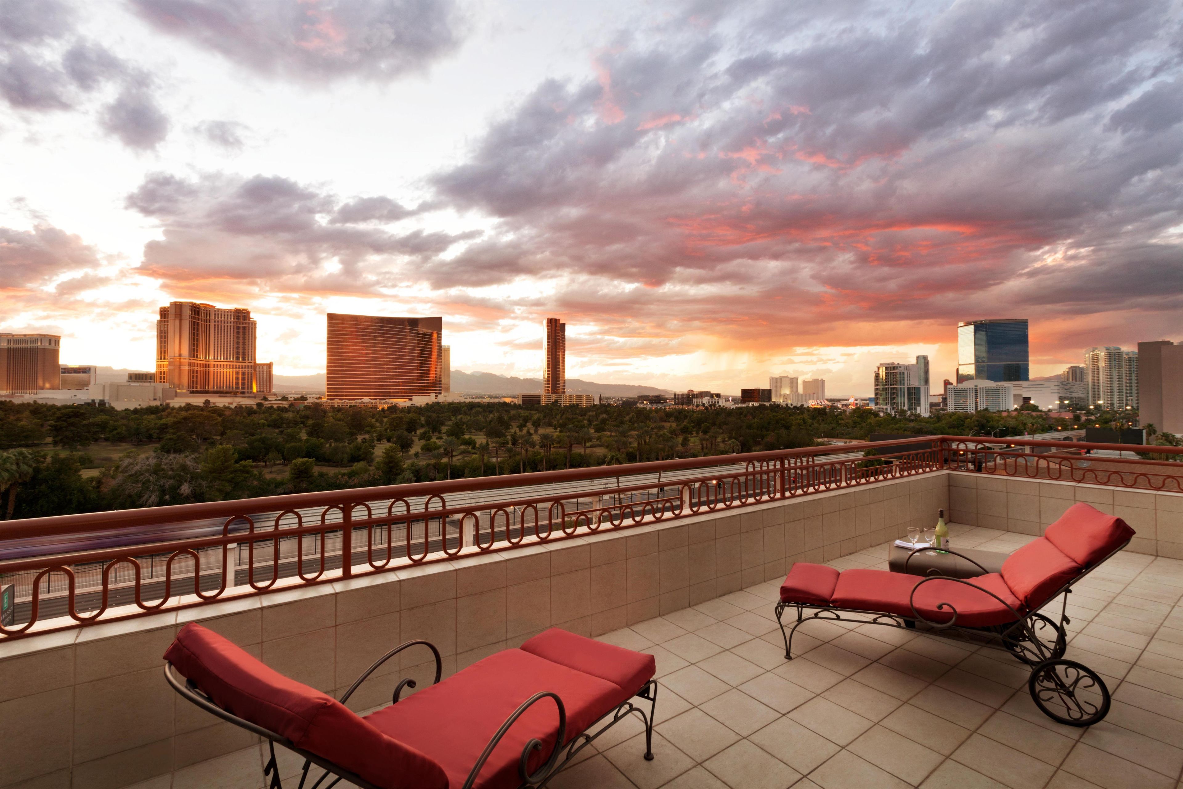 Une terrasse sur le toit, avec des fauteuils rouges et une vue sur les toits d’une ville au coucher du soleil.