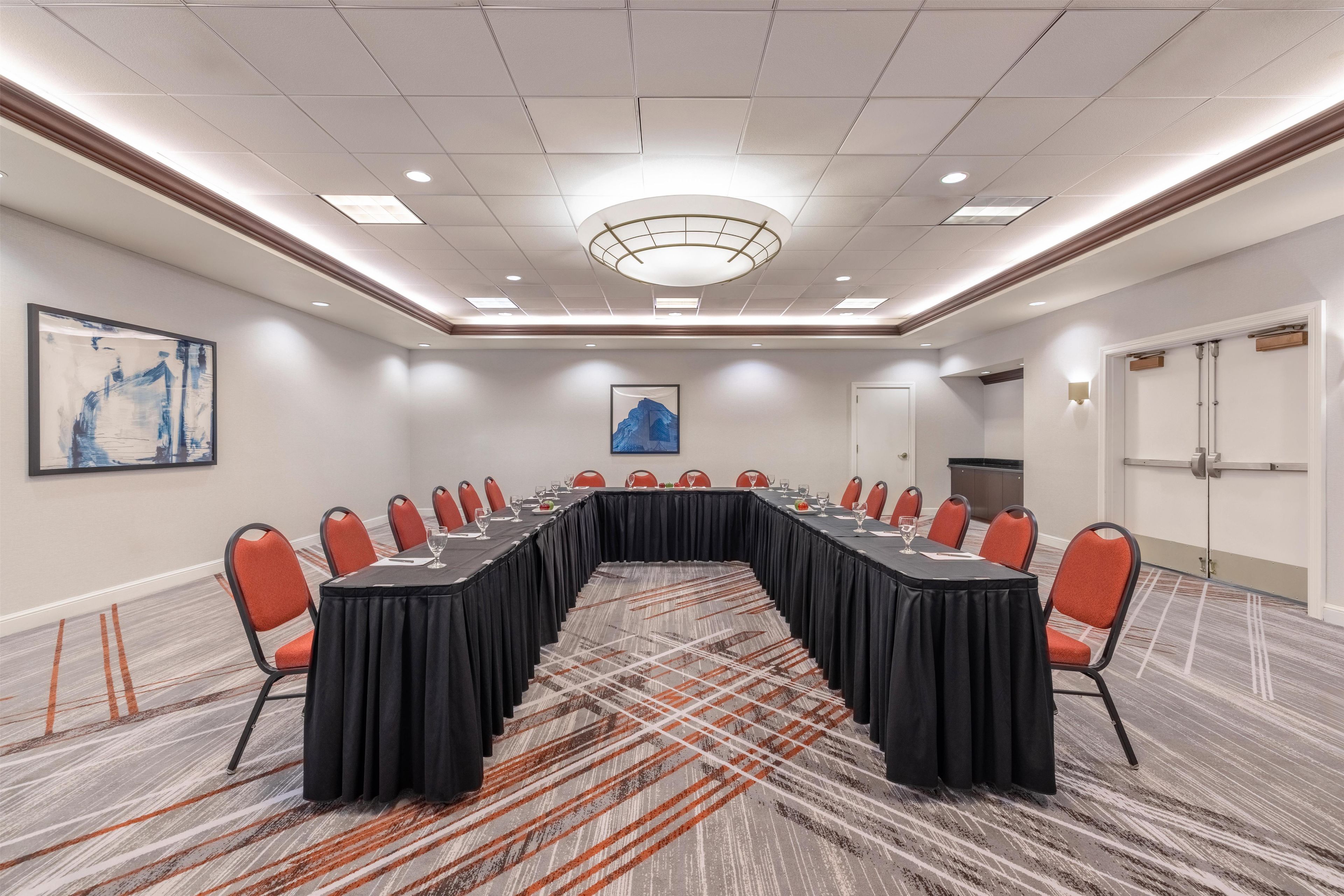 A conference room with a long table, red chairs, and a carpeted floor.