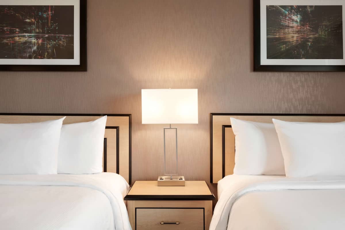 Een hotelkamer met twee bedden, een nachtkastje met een lamp, en twee ingelijste foto’s aan de muur.