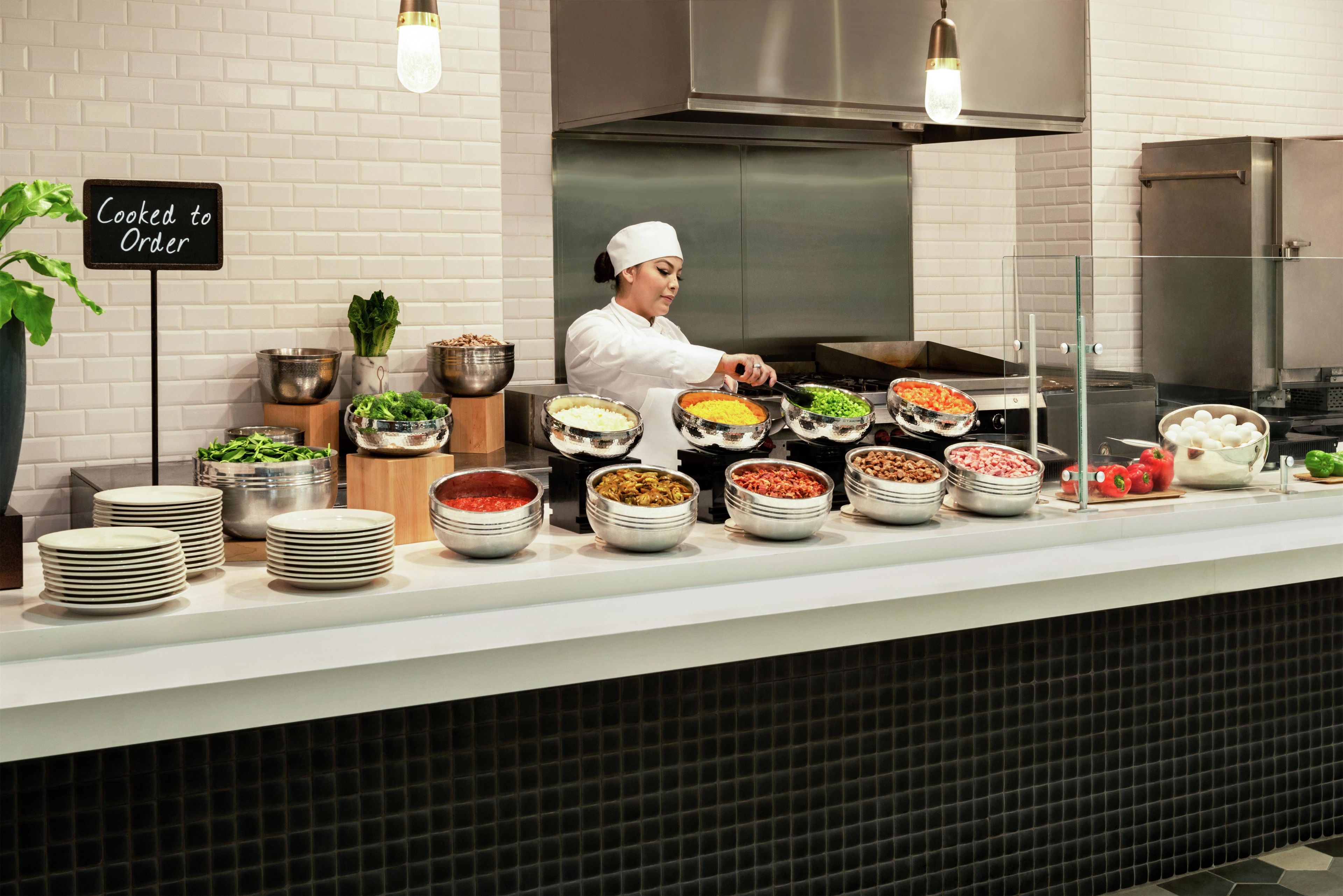 Montaje de buffet con diferentes opciones de comida y un letrero que dice 'Cocinado al momento'.