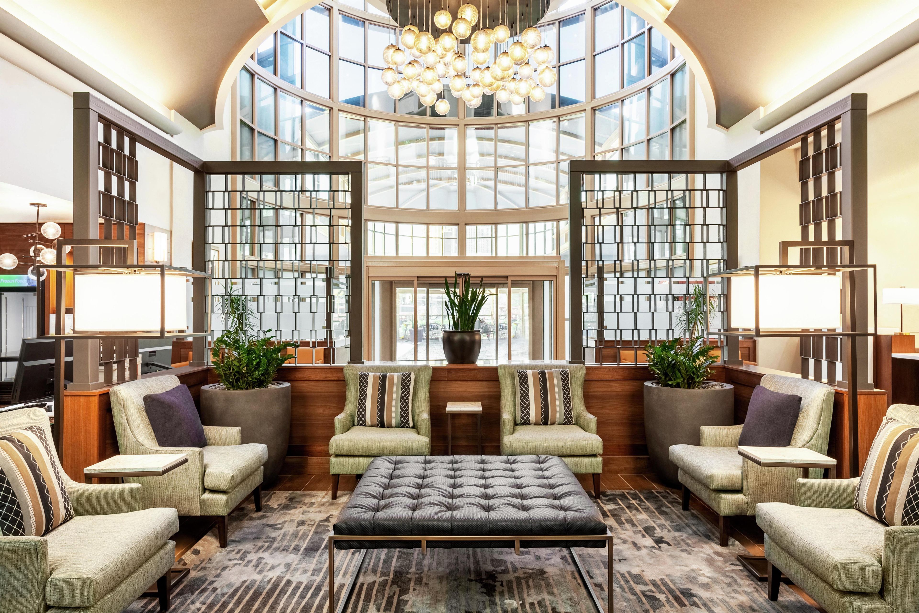 A spacious lobby with a high ceiling, large windows, and a central seating area with sofas and a coffee table.