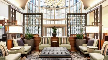 A spacious lobby with a high ceiling, large windows, and a central seating area with sofas and a coffee table.