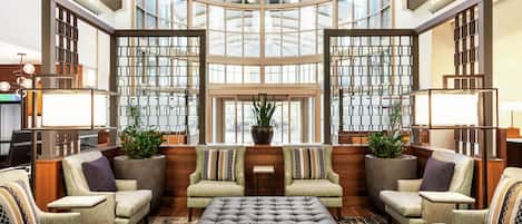 Un vestíbulo amplio con techos altos, ventanas grandes y una zona de estar central con sofás y una mesa de centro.