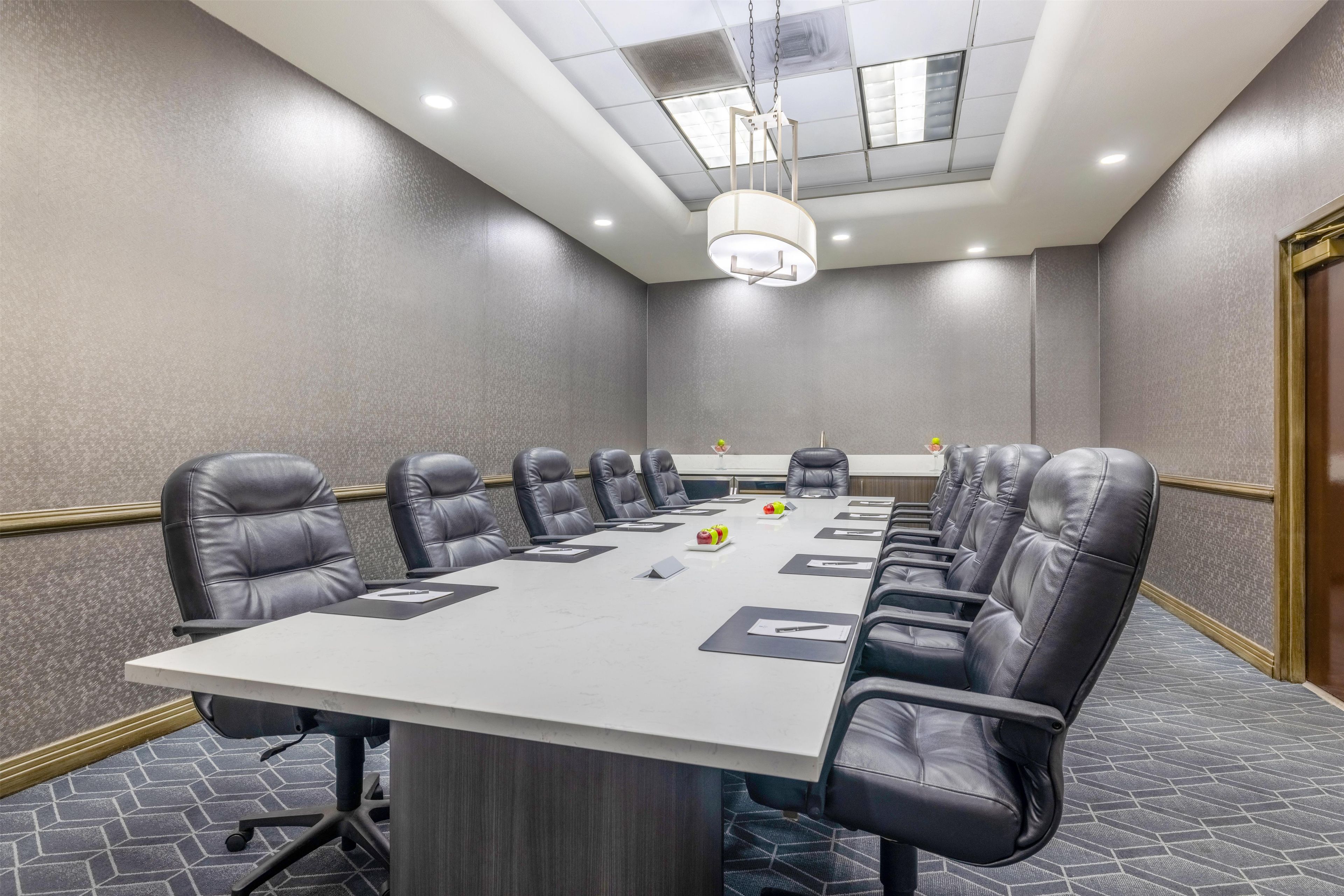 A conference room with a long table, multiple chairs, and a ceiling light fixture.