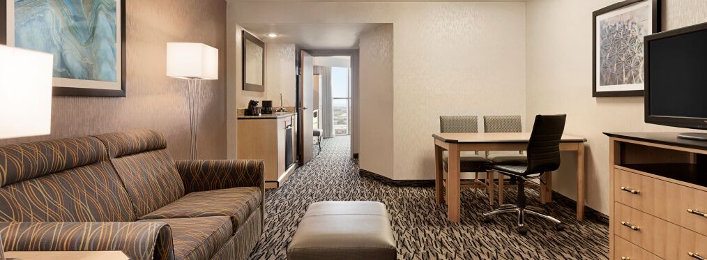 A hotel room with a sofa, a desk with a chair, a television, and a view of the city.