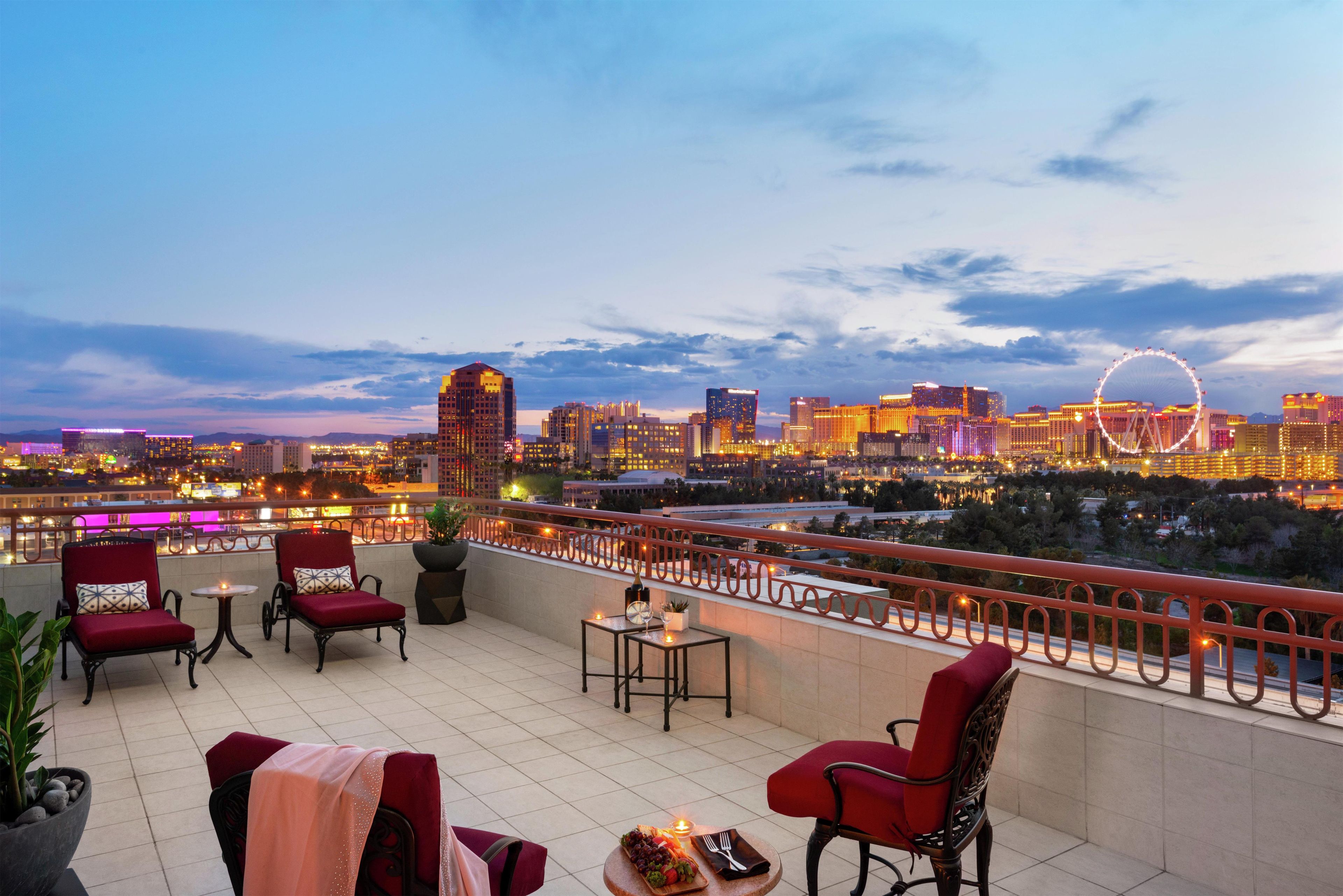 A rooftop terrace with seating and a view of a city skyline at dusk.