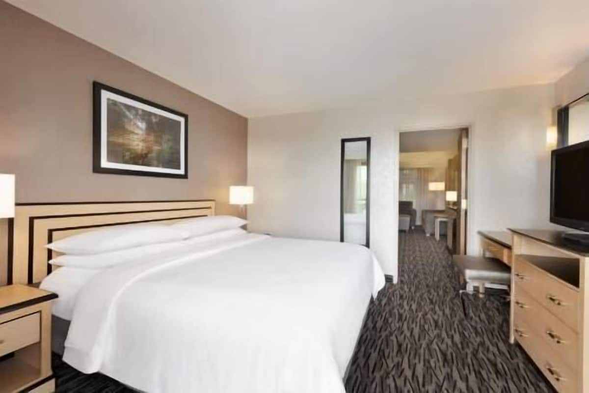 Een hotelkamer met een bed, nachtkastjes, een televisie, een spiegel en een gang die naar een badkamer leidt.