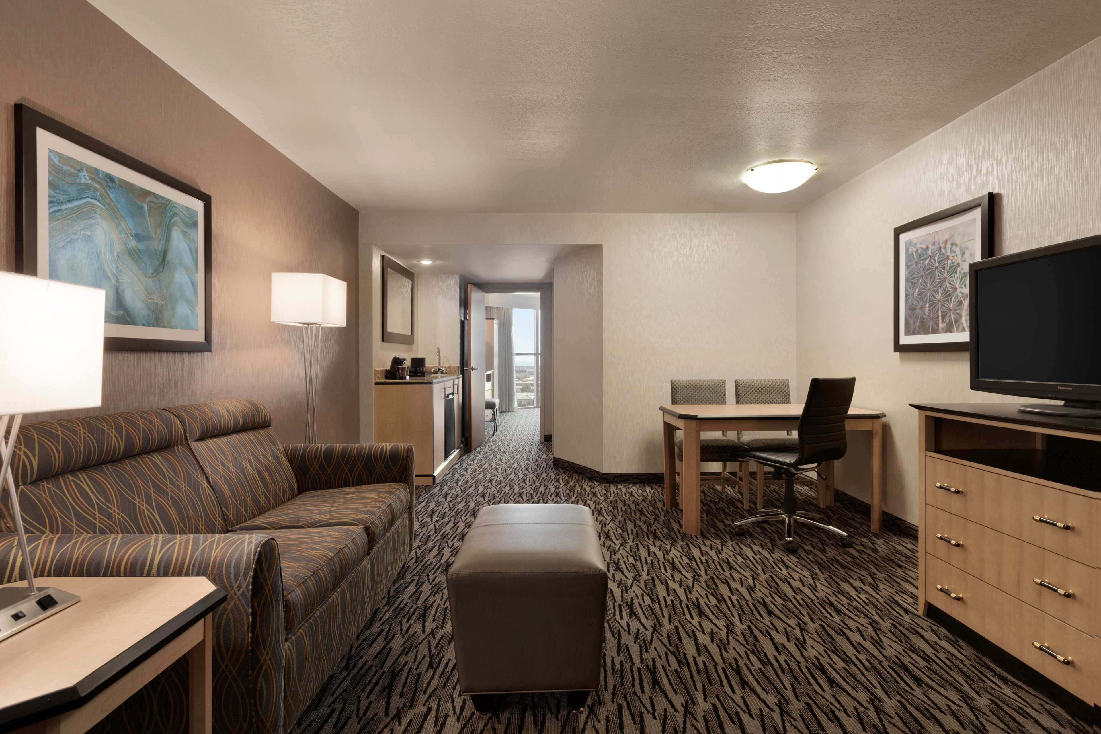 Una habitación de hotel con sofá, escritorio, televisor y piso alfombrado.